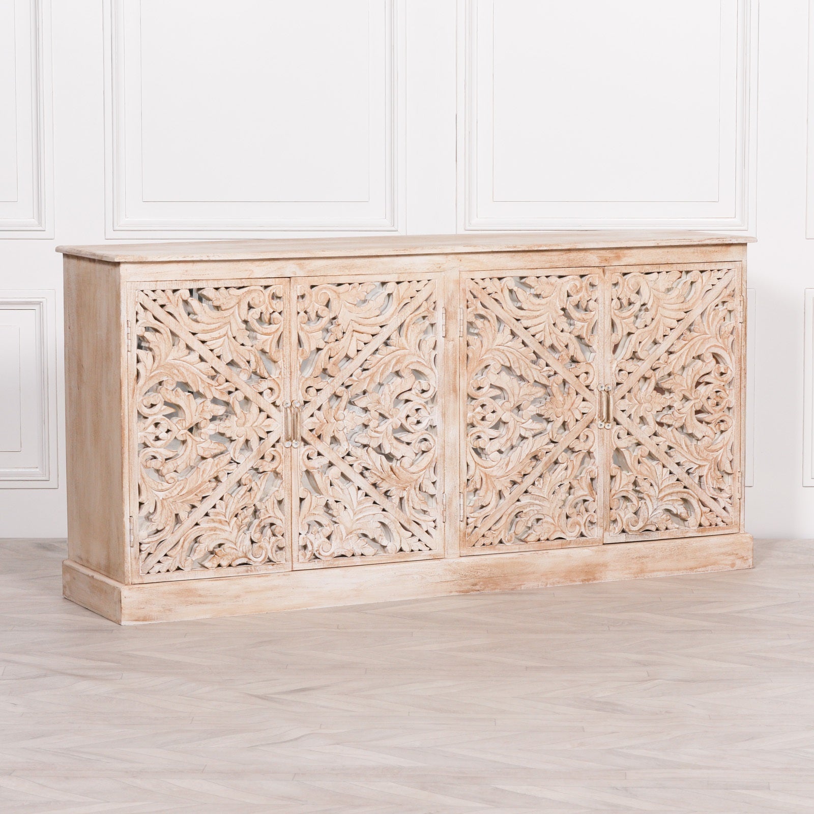Perspective view of the Camille Four Door Carved Mirrored Sideboard in bleached mango wood showcasing handcrafted carved mirrored doors, artisan detailing and elegant storage cabinet design.