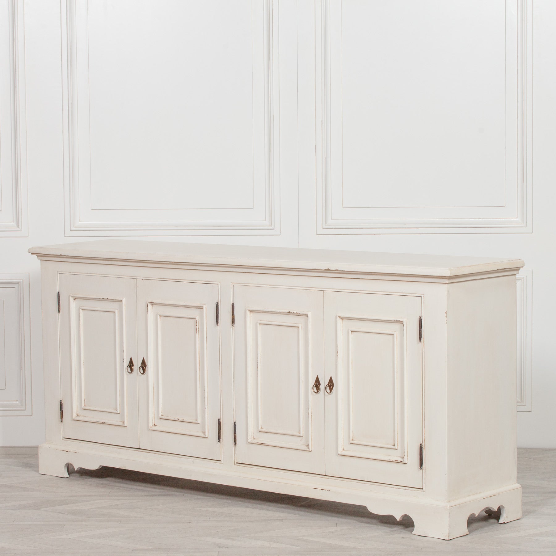 Angled view of the Camille Four Door Classical Sideboard in an aged white mahogany finish with traditional panelled cupboard doors, handcrafted construction and generous storage for dining rooms, living rooms and hallways.