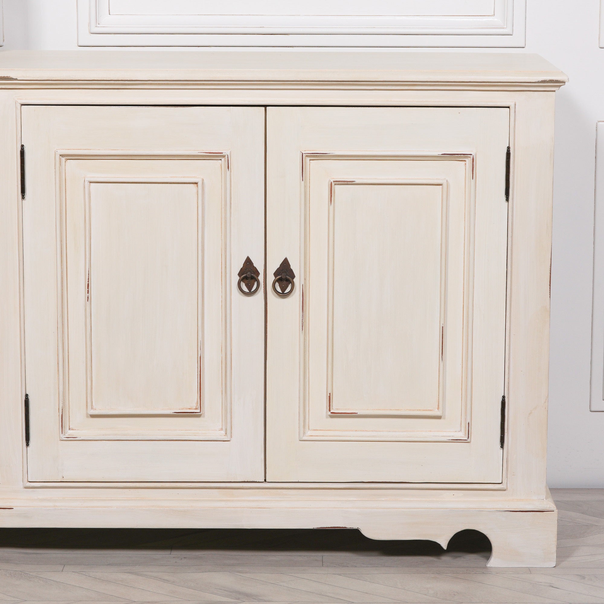 Close-up of the Camille Four Door Classical Sideboard displaying the aged white painted mahogany finish, panelled cupboard doors, antique ring pull handles and traditional handcrafted cabinet design.