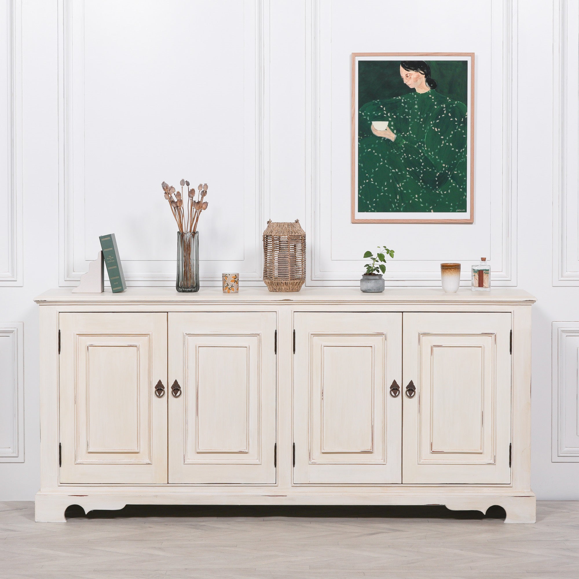 Camille Four Door Classical Sideboard styled with decorative accessories beneath framed wall art, featuring an aged white mahogany finish and versatile storage for elegant living rooms, dining rooms or hallways.