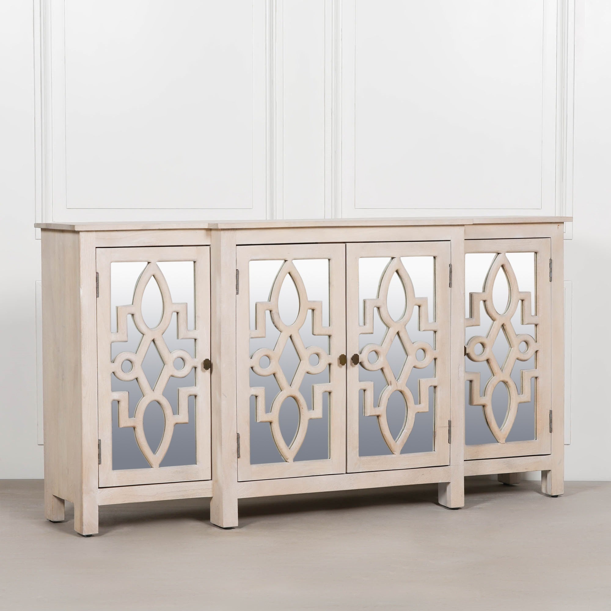 Angled view of the Camille Four Door Mirrored Sideboard in bleached mango wood highlighting mirrored door panels, handcrafted construction and stylish storage for living rooms, dining rooms and hallways.