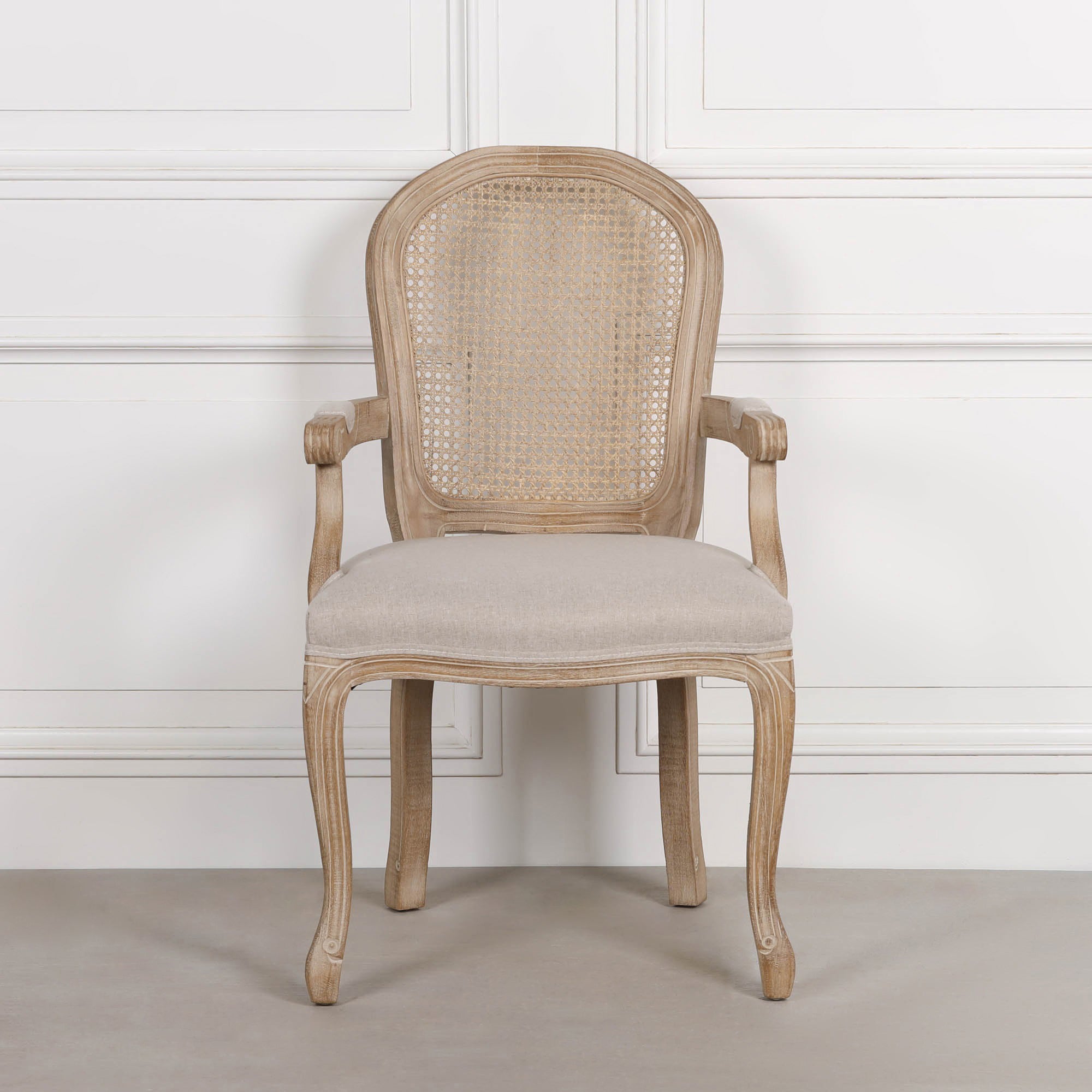 Front view of Camille French Louis birch wood dining armchair with cane back and linen seat against a white panelled wall