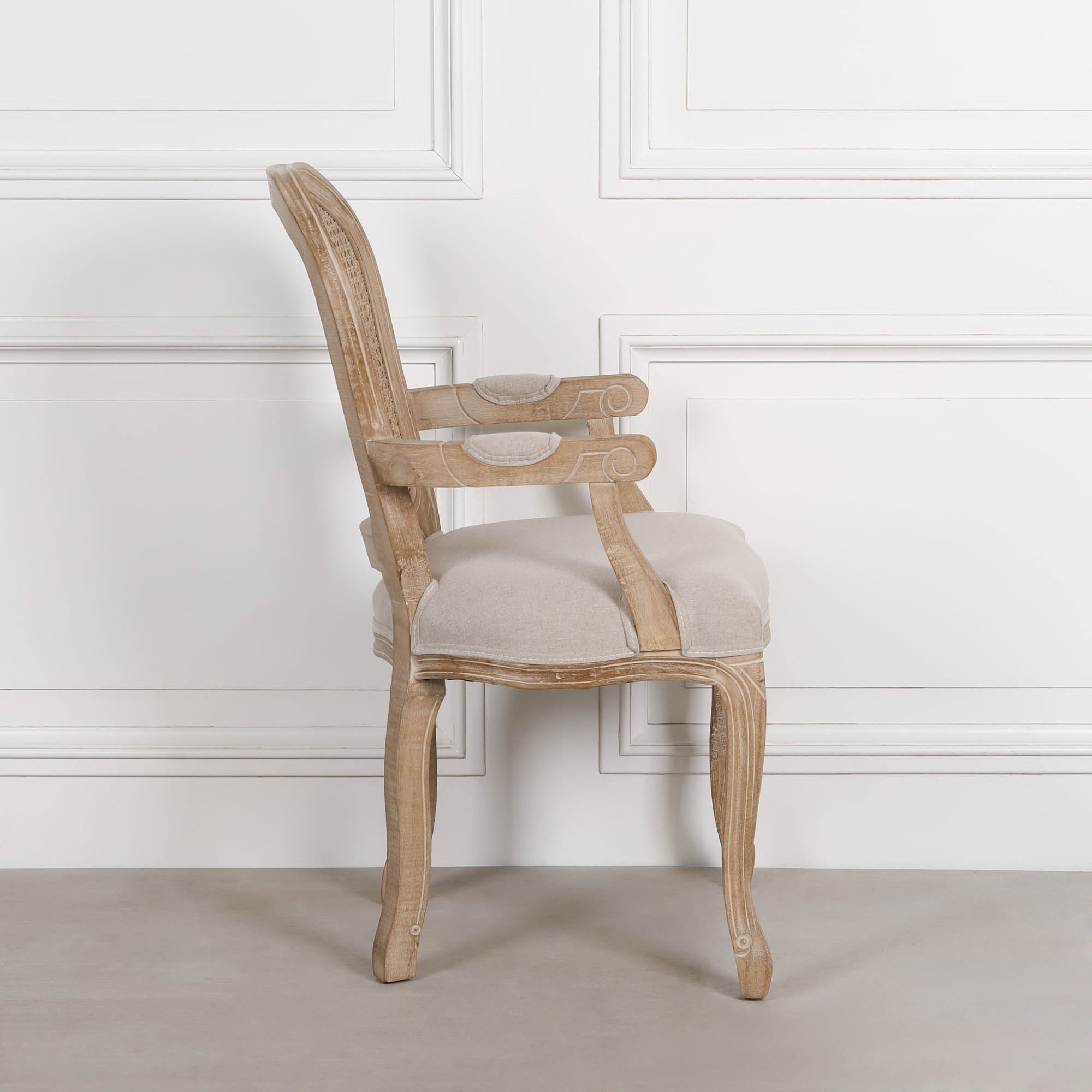 Side view of Camille French Louis cane back dining armchair with linen seat against a white panelled wall