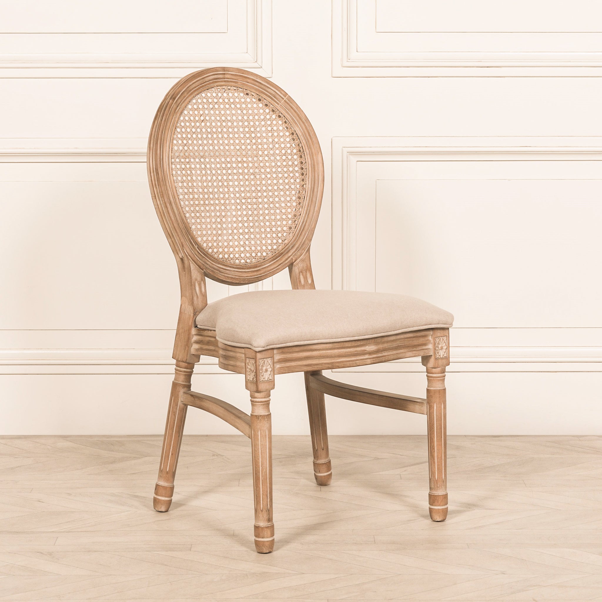 Angled front view of the Camille French Louis Linen Upholstered Dining Chair with carved wooden frame, woven rattan backrest and linen upholstered seat styled within a bright French-inspired interior.