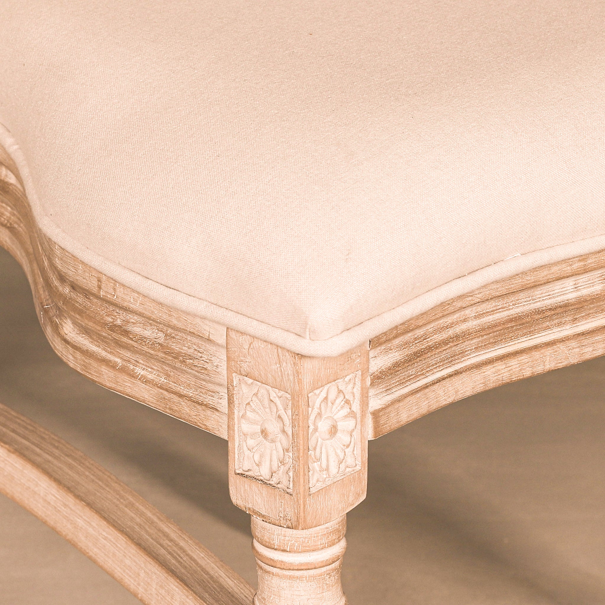 Close-up of the Camille French Louis Linen Upholstered Dining Chair with Light Washed Wood Frame highlighting the linen seat cushion, hand-carved floral corner detailing, turned leg and light washed wood finish.