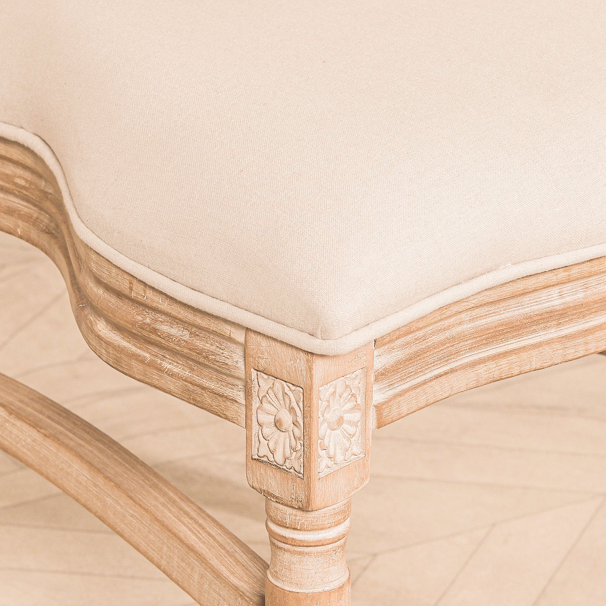 Detailed view of the Camille French Louis Linen Upholstered Dining Chair with Light Washed Wood Frame showcasing the linen seat cushion, carved floral corner blocks, shaped wooden apron and handcrafted Louis-style construction.