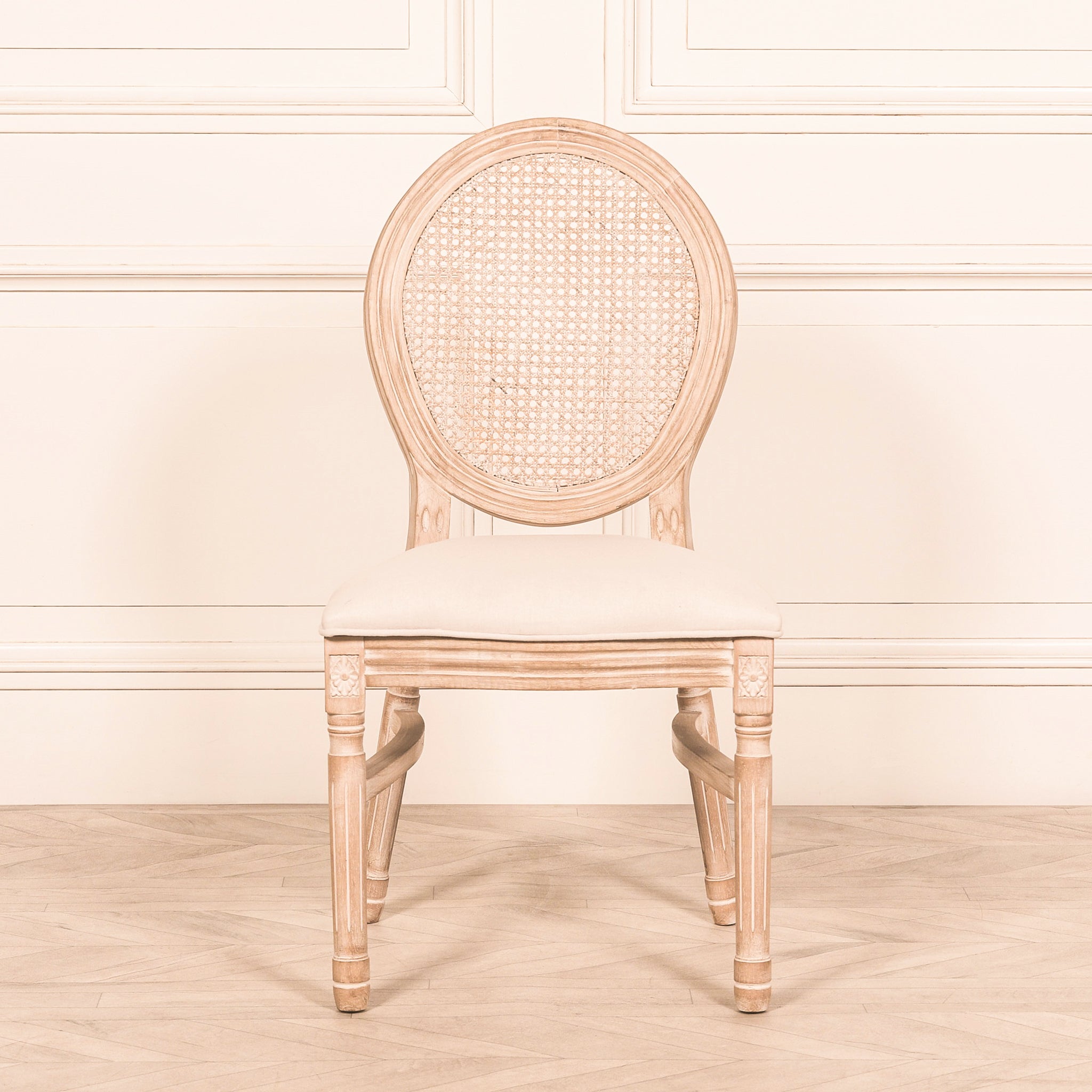 Front view of the Camille French Louis Linen Upholstered Dining Chair with Light Washed Wood Frame featuring a handwoven rattan backrest, carved wooden legs, upholstered linen seat and timeless French country dining room design.