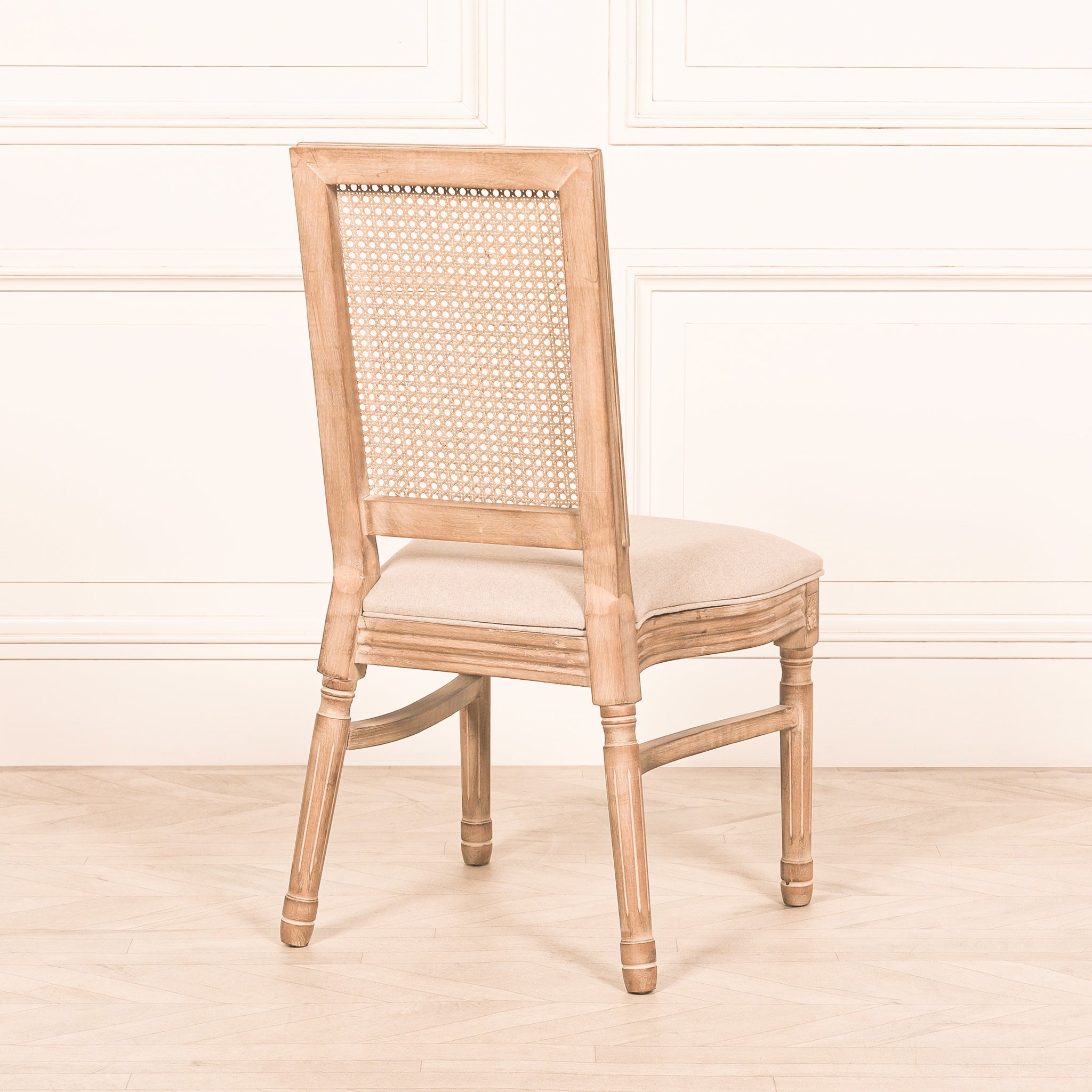 Rear view of the Camille French Louis Rattan Back Dining Chair featuring a woven natural rattan backrest, carved wooden legs and linen upholstered seat in a bright interior.