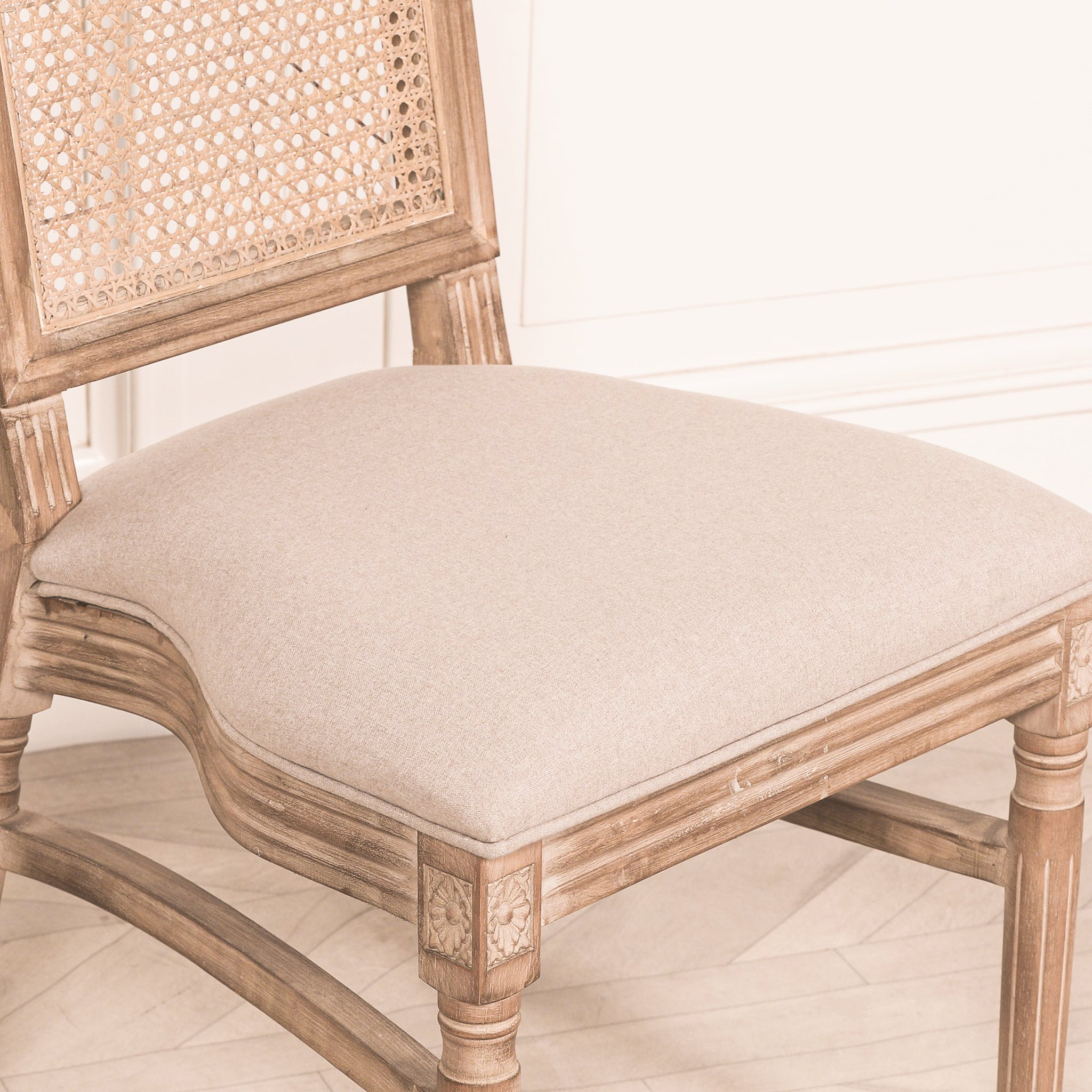 Close-up of the Camille French Louis Rattan Back Dining Chair showing the premium linen upholstered seat, carved wooden apron and woven rattan backrest.
