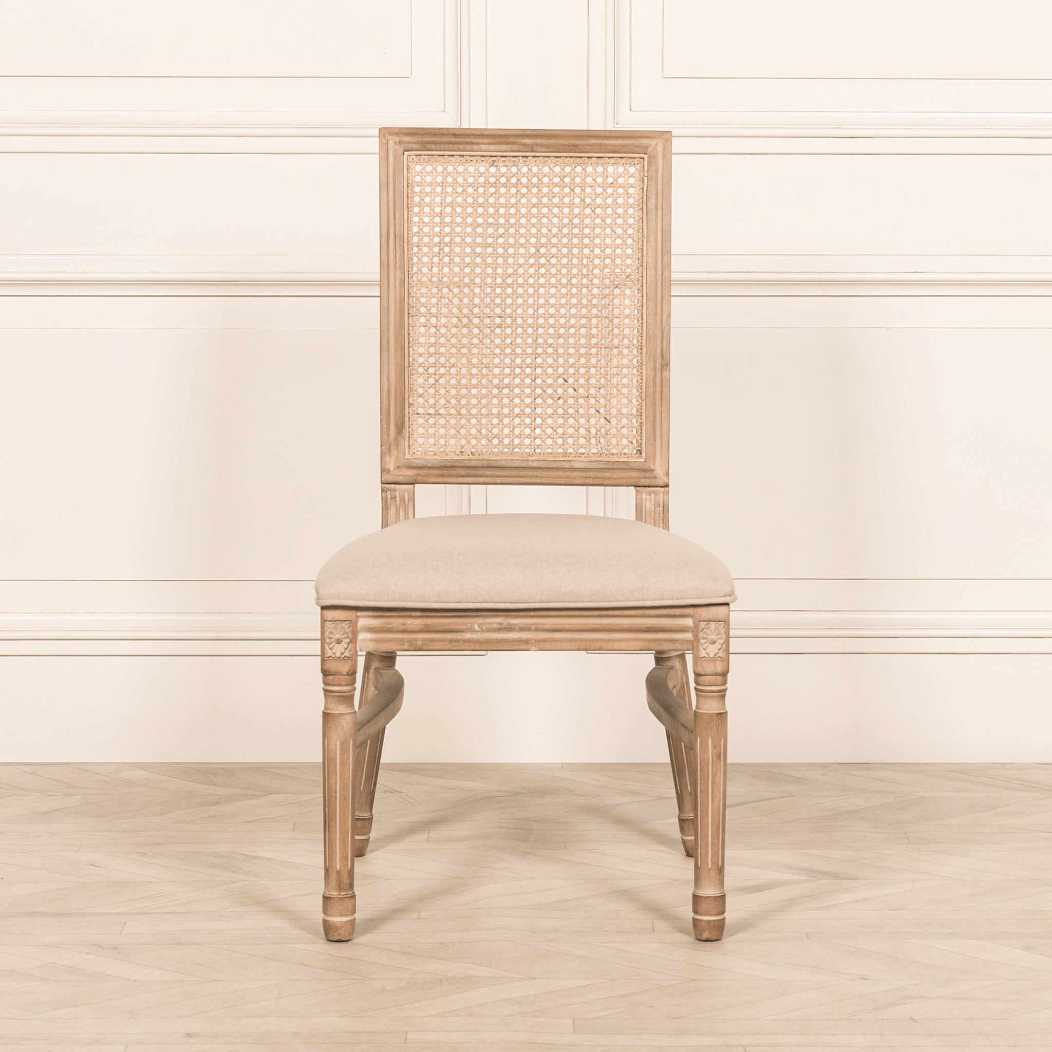 Camille French Louis Rattan Back Dining Chair with linen upholstered seat, natural carved wooden frame and woven rattan backrest shown from the front in a French country style dining room.