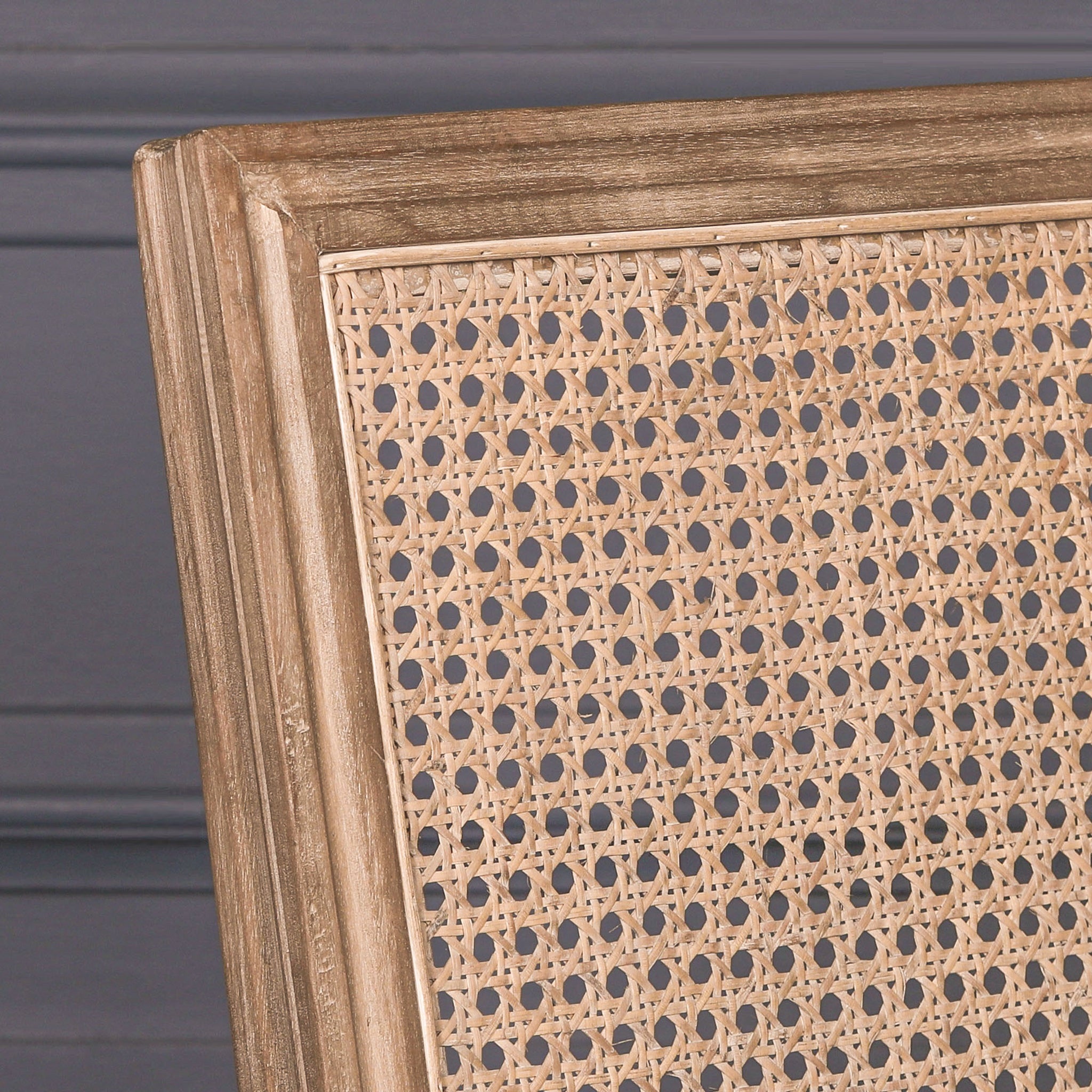 Detailed close-up of the Camille French Louis Rattan Back Dining Chair showcasing the woven natural rattan backrest and carved wooden frame against a dark panelled background.
