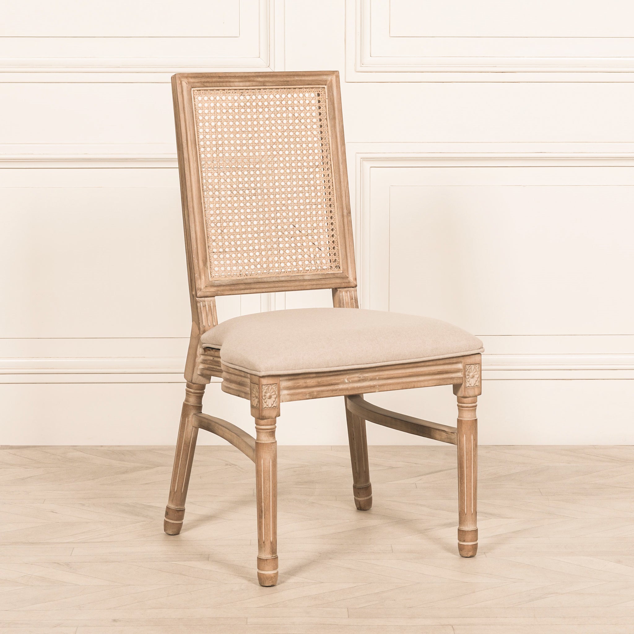 Three-quarter view of the Camille French Louis Rattan Back Dining Chair featuring a woven rattan backrest, carved wooden legs and soft linen upholstered seat in a bright French-inspired interior.