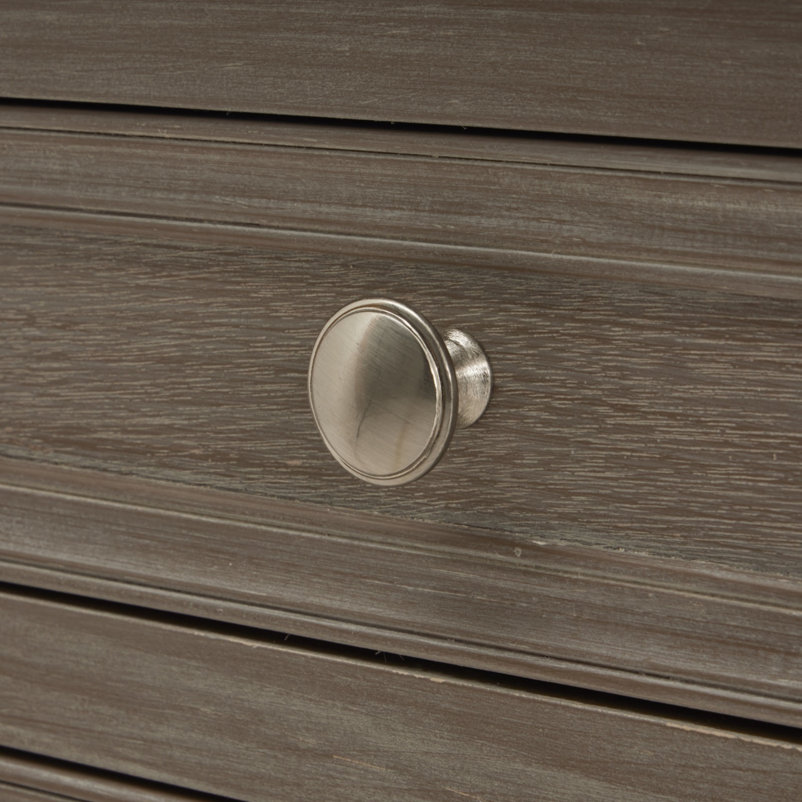 Close-up of silver knob and grey wood grain on Camille bedside table drawer against a neutral background.