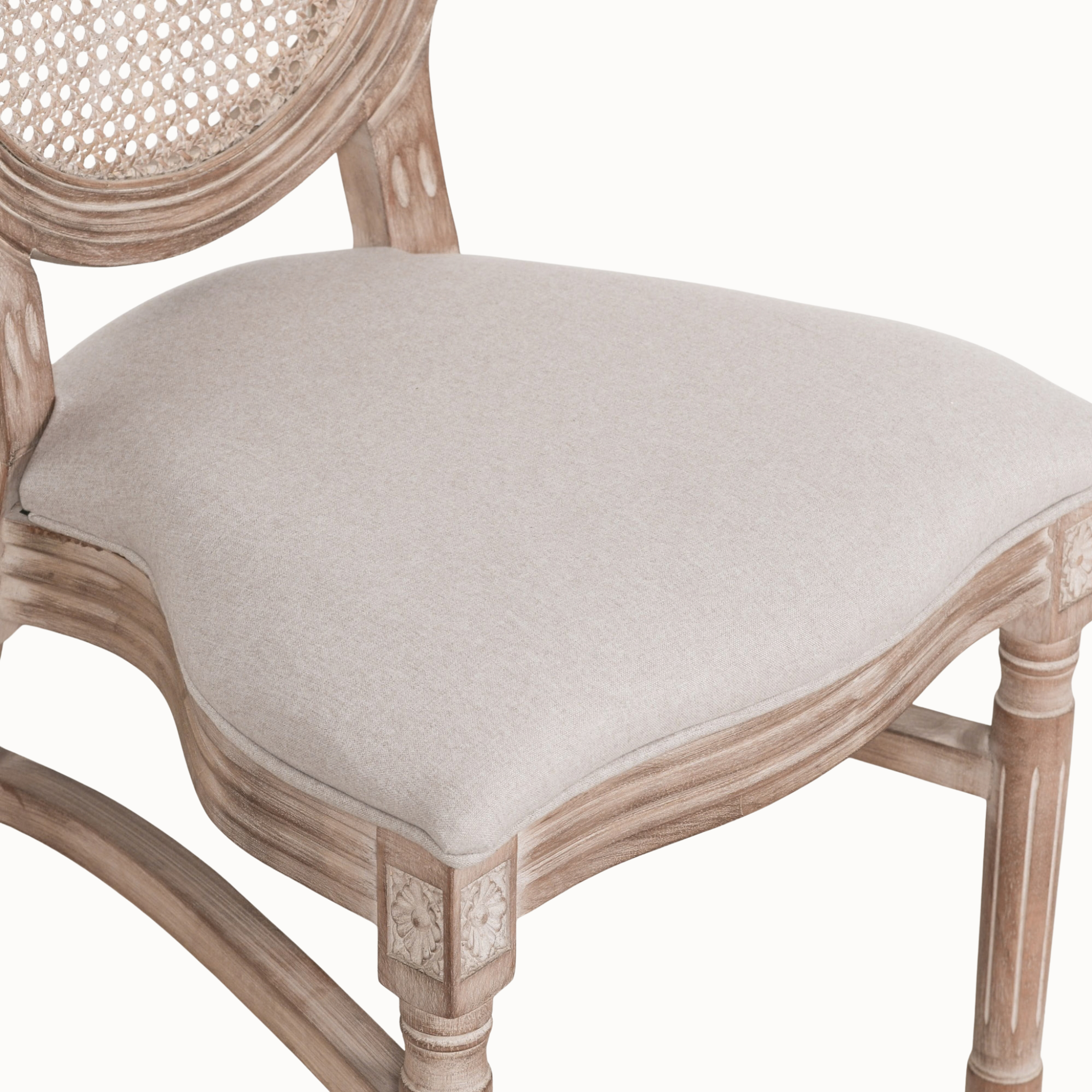 Close-up of Camille dining chair showing linen upholstered seat, carved wood frame and cane back on white.