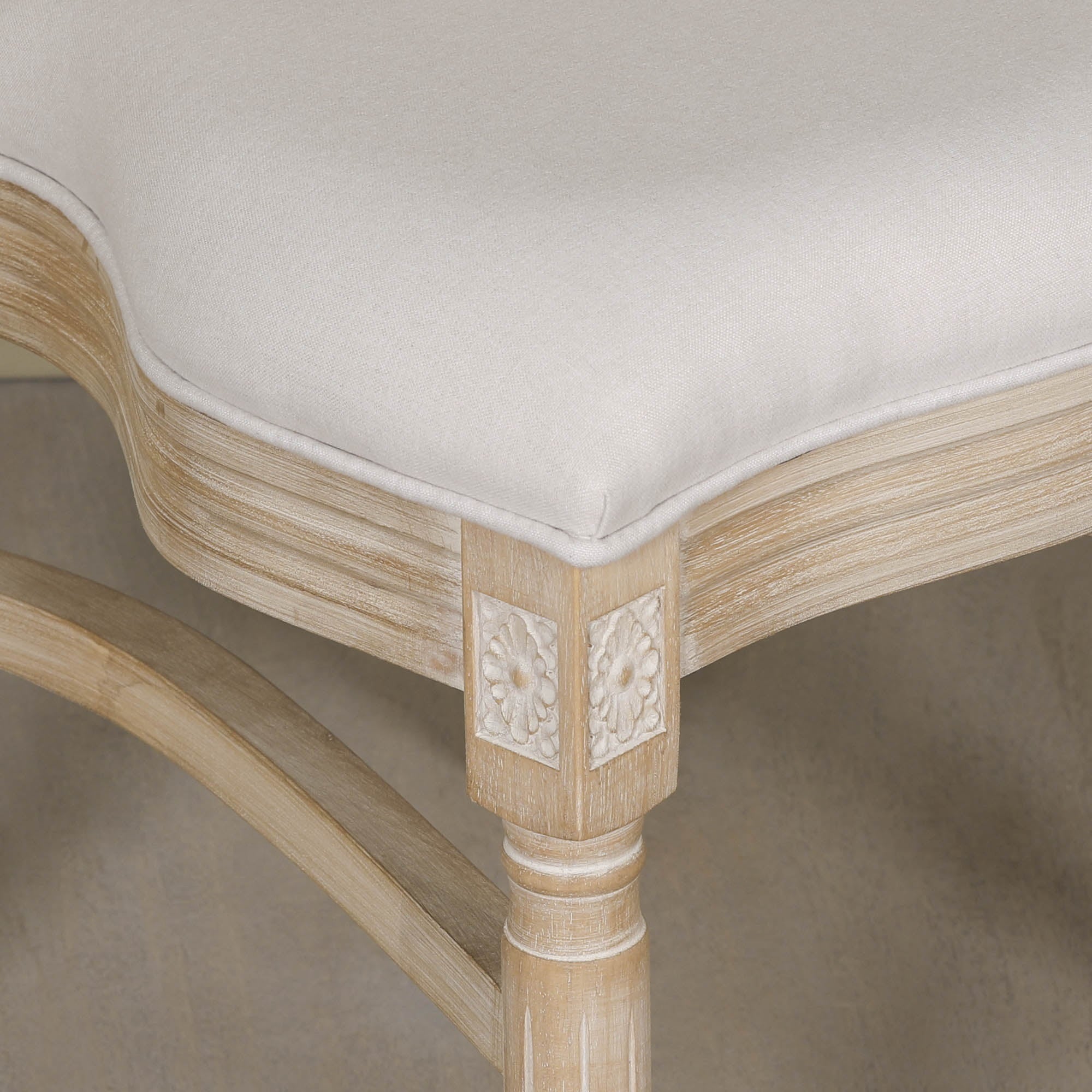 Close-up of Camille linen dining chair seat and light washed wood frame with carved floral detail on a neutral background.