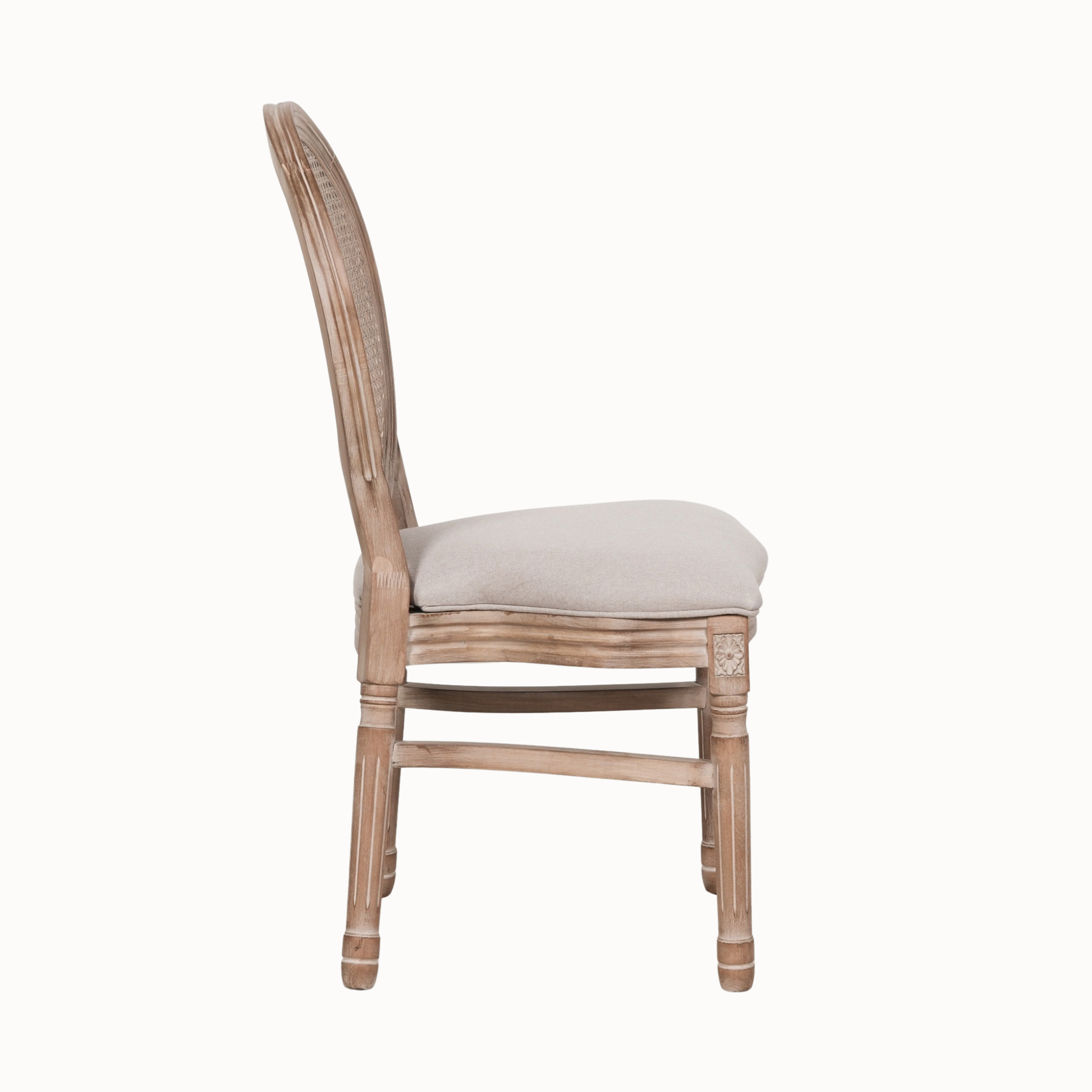 Side view of Camille linen upholstered dining chair with carved wood frame and cane back on white.