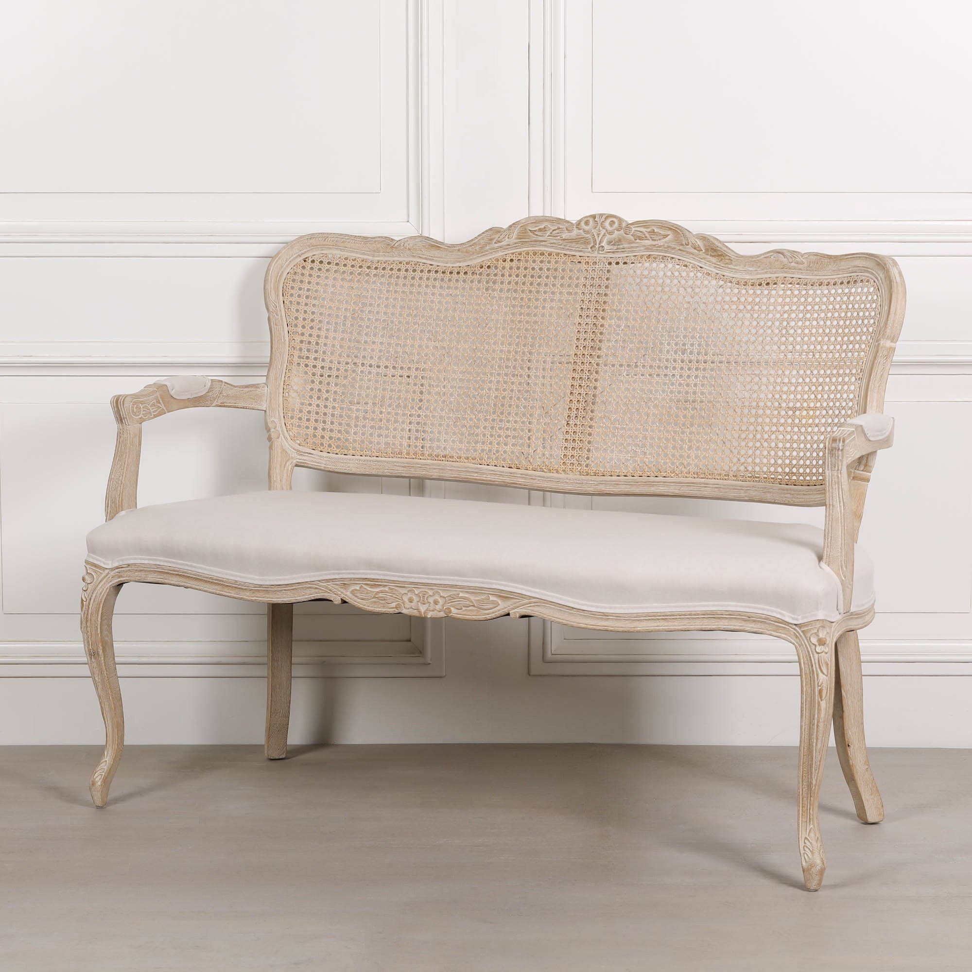 Angled view of Camille Louis 2 seater settee with carved birch wood frame, cane back and cream linen seat.