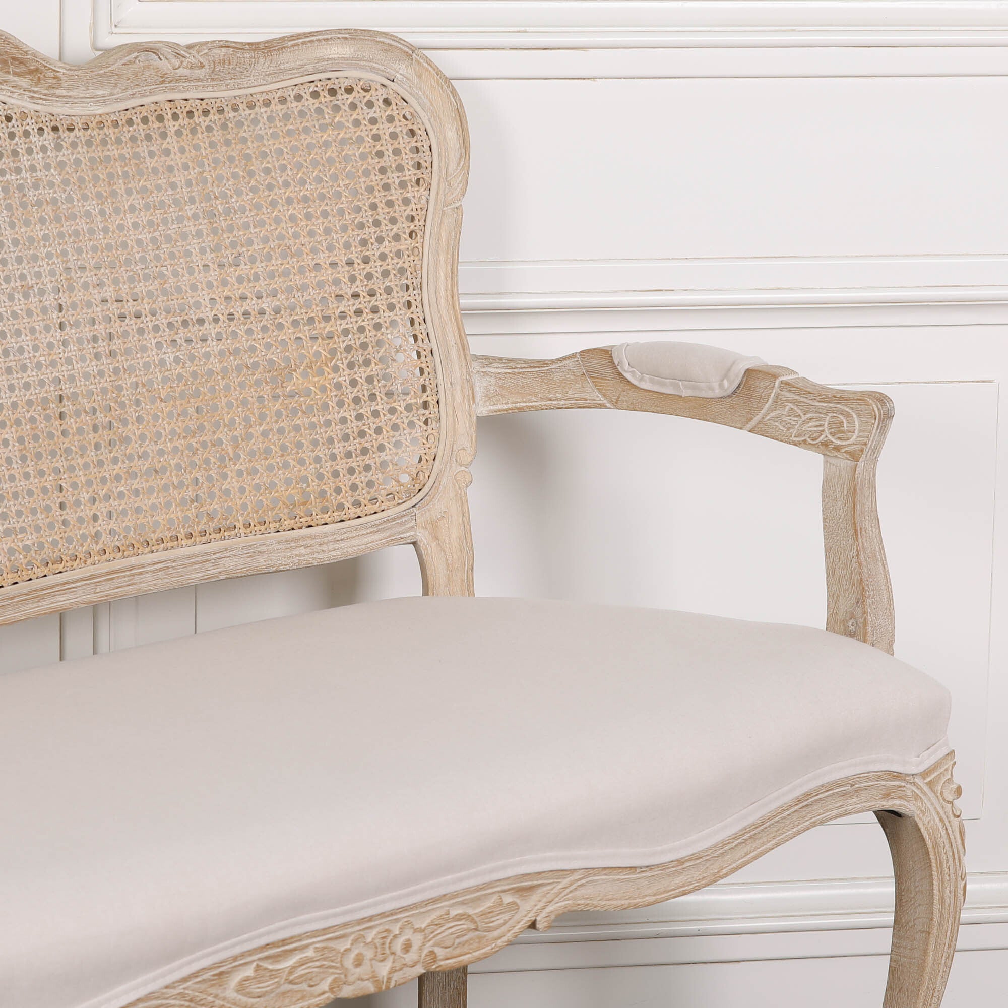 Close-up of Camille Louis 2 seater settee with cane back, cream linen upholstery and carved birch wood arm.