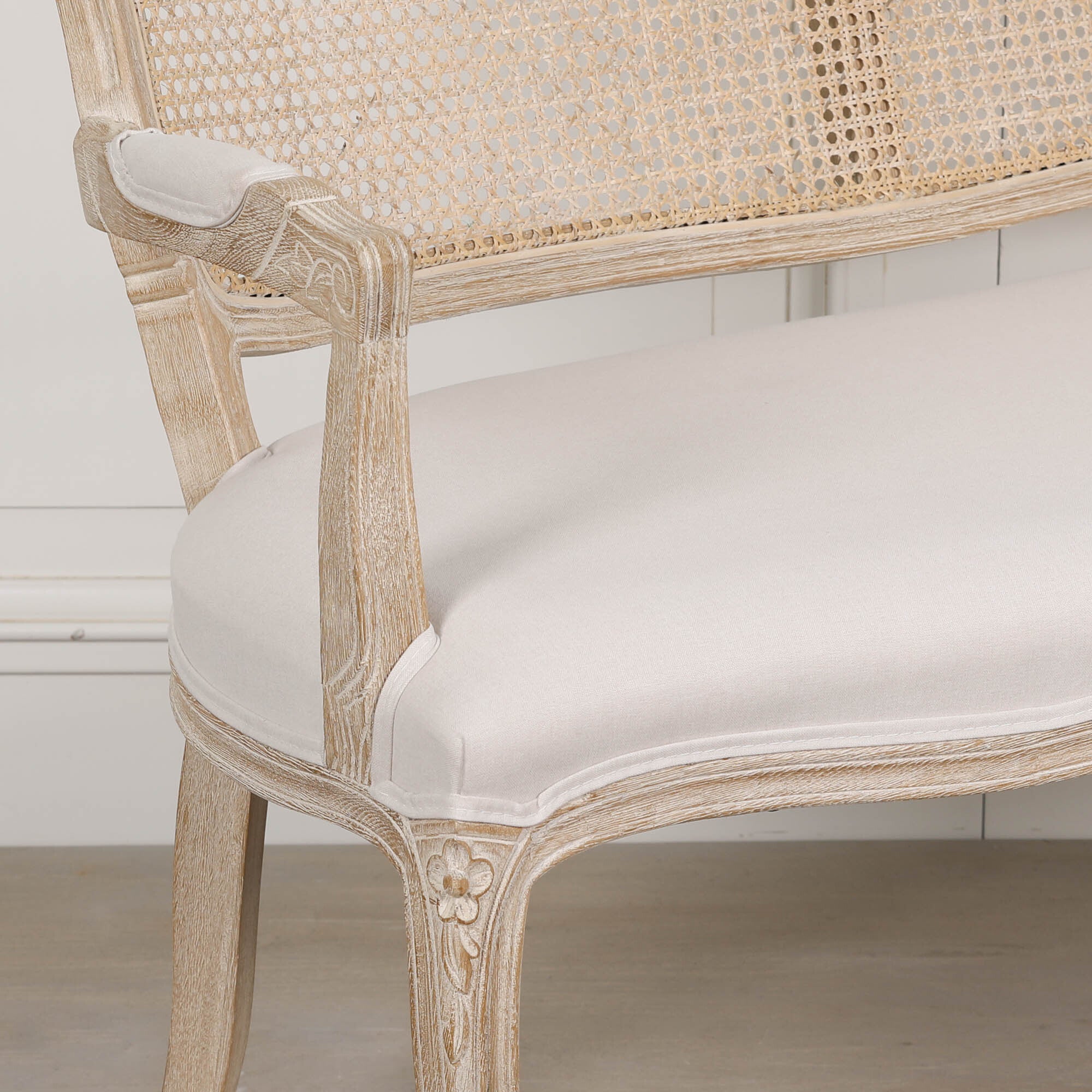Close-up of Camille Louis settee with natural cane back, cream linen seat and carved birch wood frame.