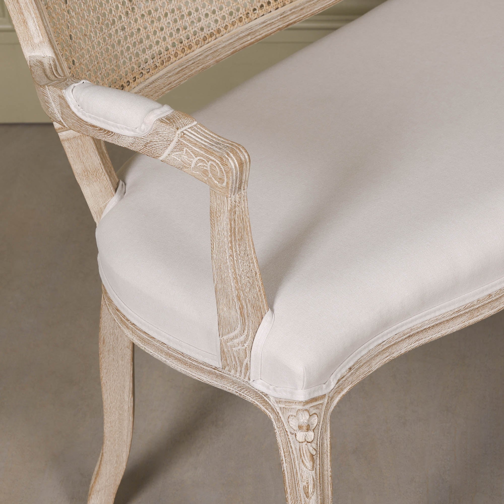 Close-up of Camille Louis settee showing cream linen upholstery, carved birch wood arm and floral leg detail.