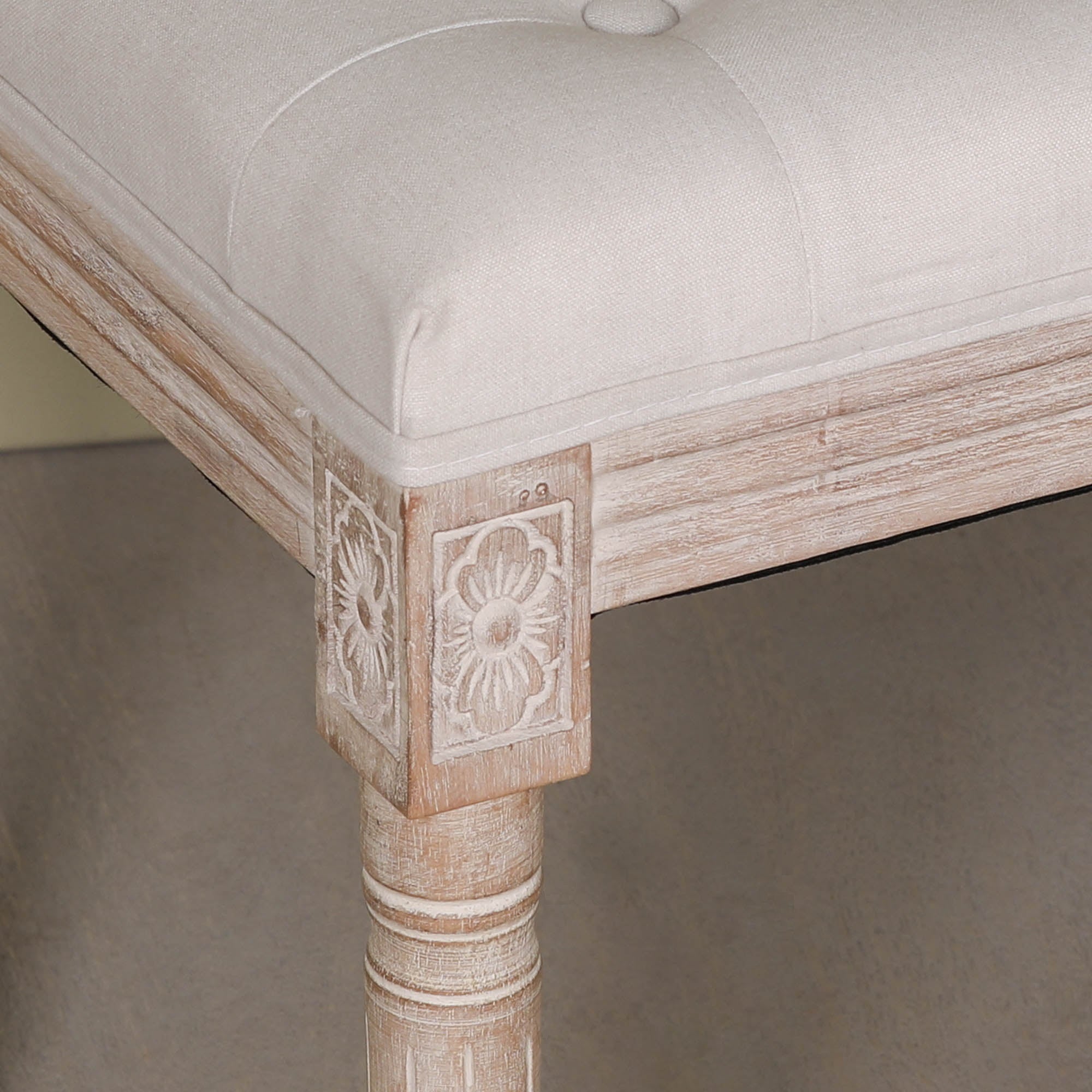 Close-up of the Camille Louis Upholstered Bench highlighting the beige button tufted linen seat, hand-carved corner detailing and turned washed birch wood leg, showcasing premium French-inspired craftsmanship.