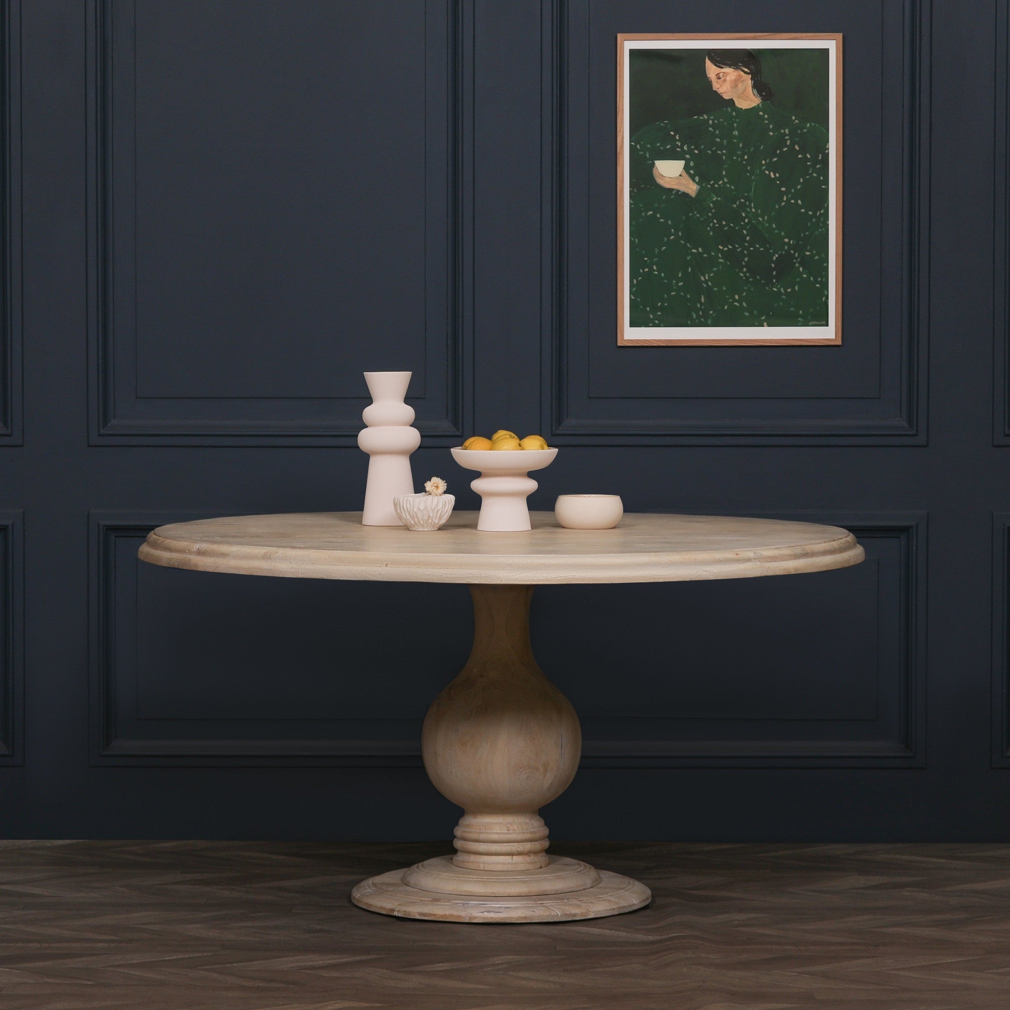 Camille Round Pedestal Dining Table 152cm for 6 in Bleached Mango Wood styled with decorative accessories against a dark panelled wall, highlighting the spacious round tabletop, sculptural pedestal base, natural wood finish and elegant contemporary dining room styling.