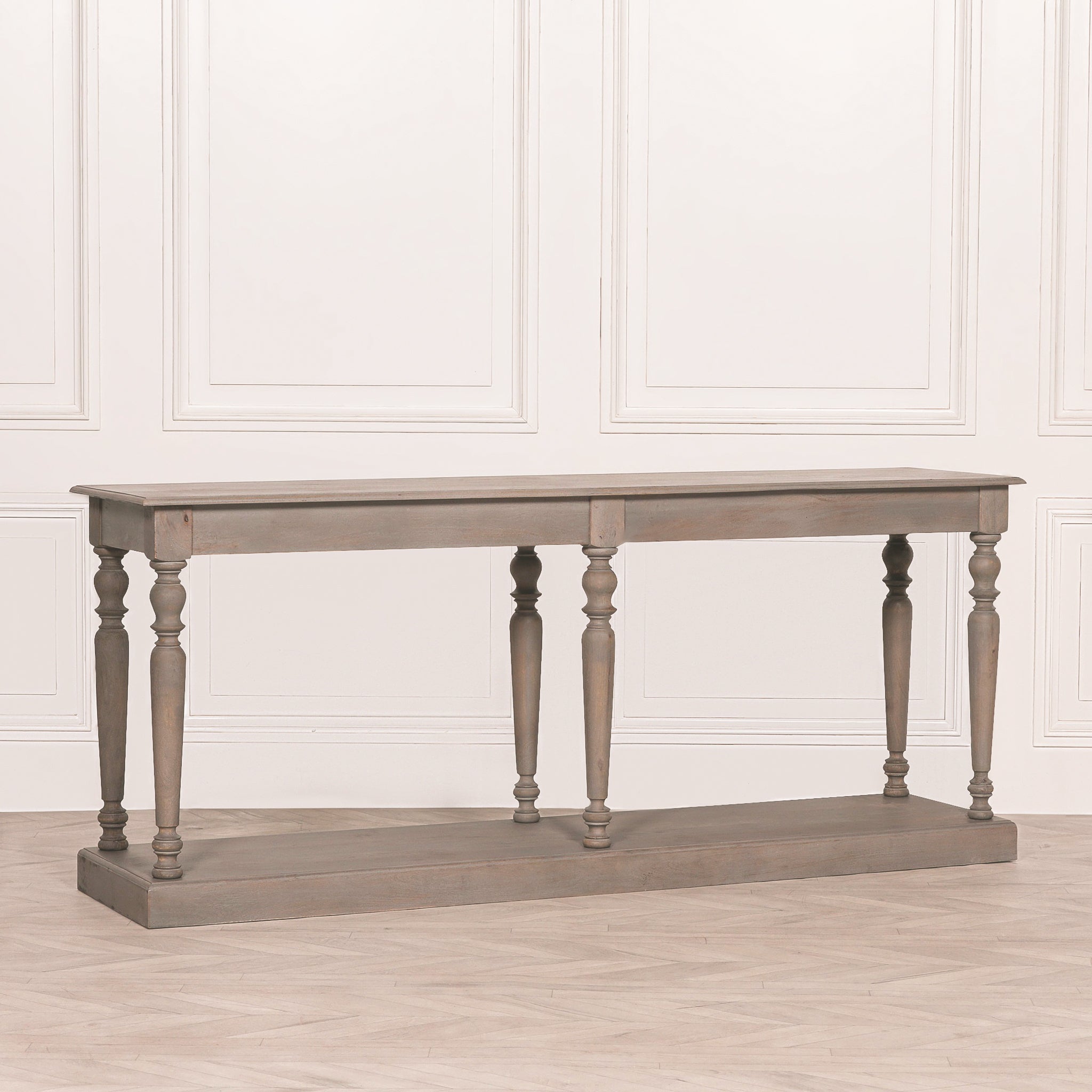 Angled view of the Camille rustic wooden console table highlighting the handcrafted turned column legs, thick rustic tabletop, generous lower storage shelf and elegant weathered wood finish.