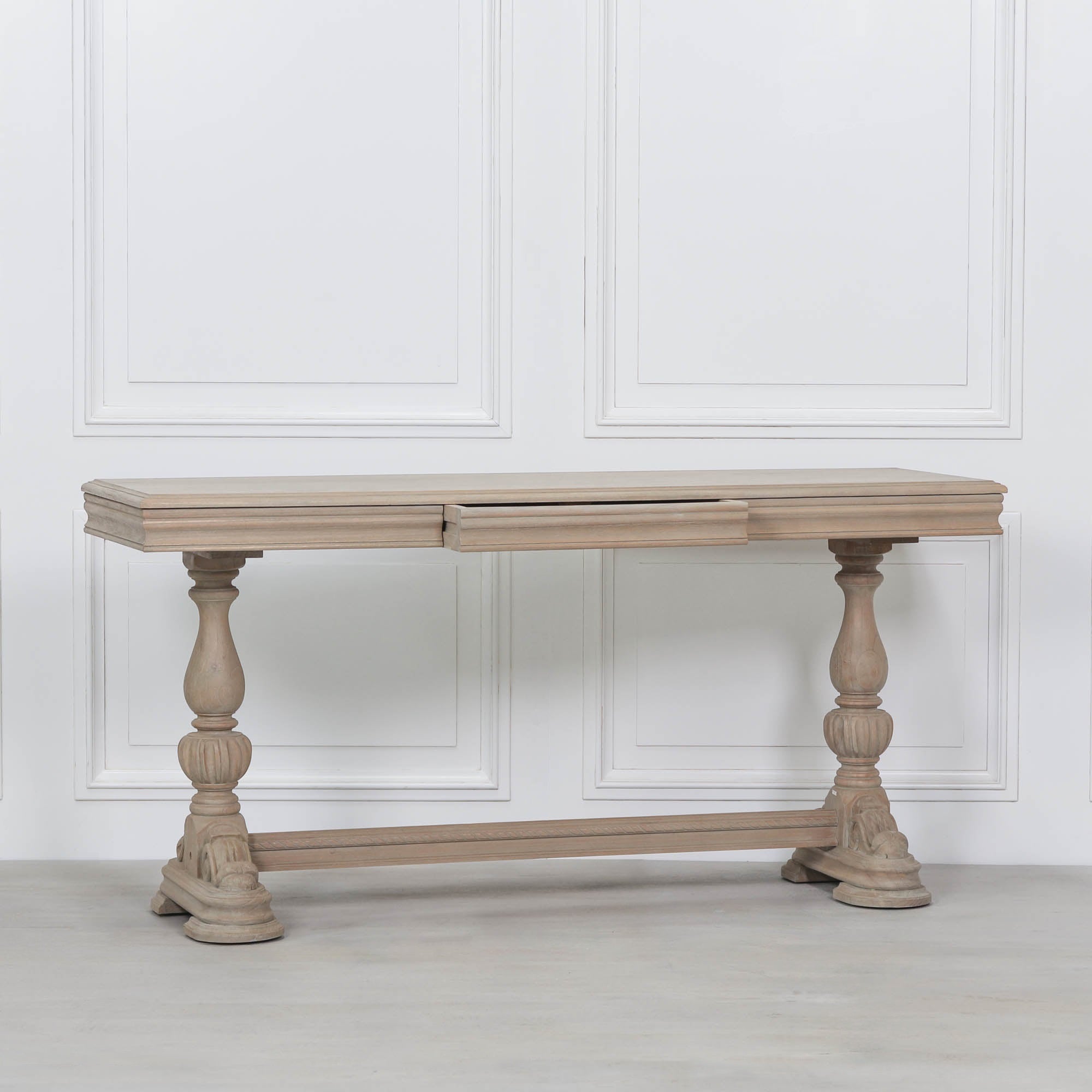 Camille rustic white cedar wood console table with drawer, carved legs and stretcher against a white panelled wall.