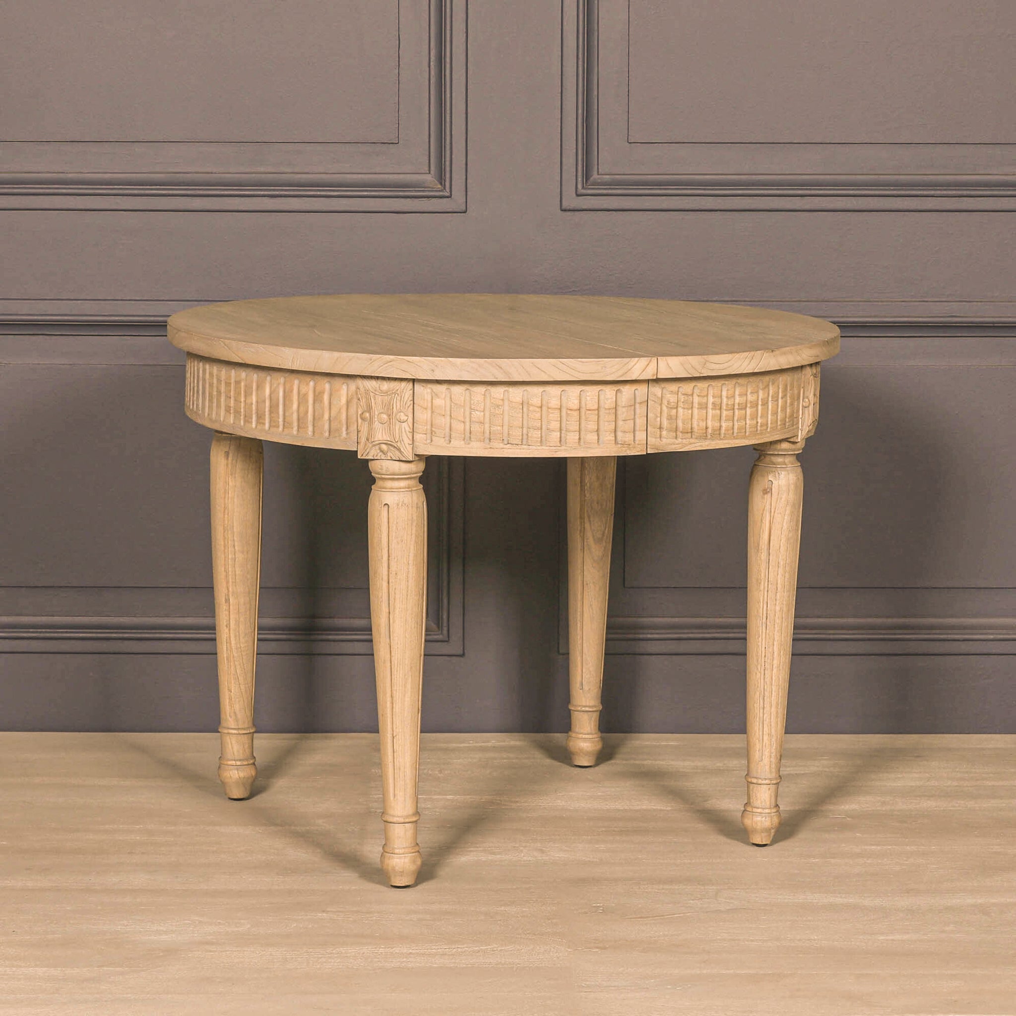 Camille White Cedar Wood Extendable Dining Table in its round 100cm configuration against a grey panelled wall, highlighting the rustic white cedar wood finish, carved apron and turned wooden legs.