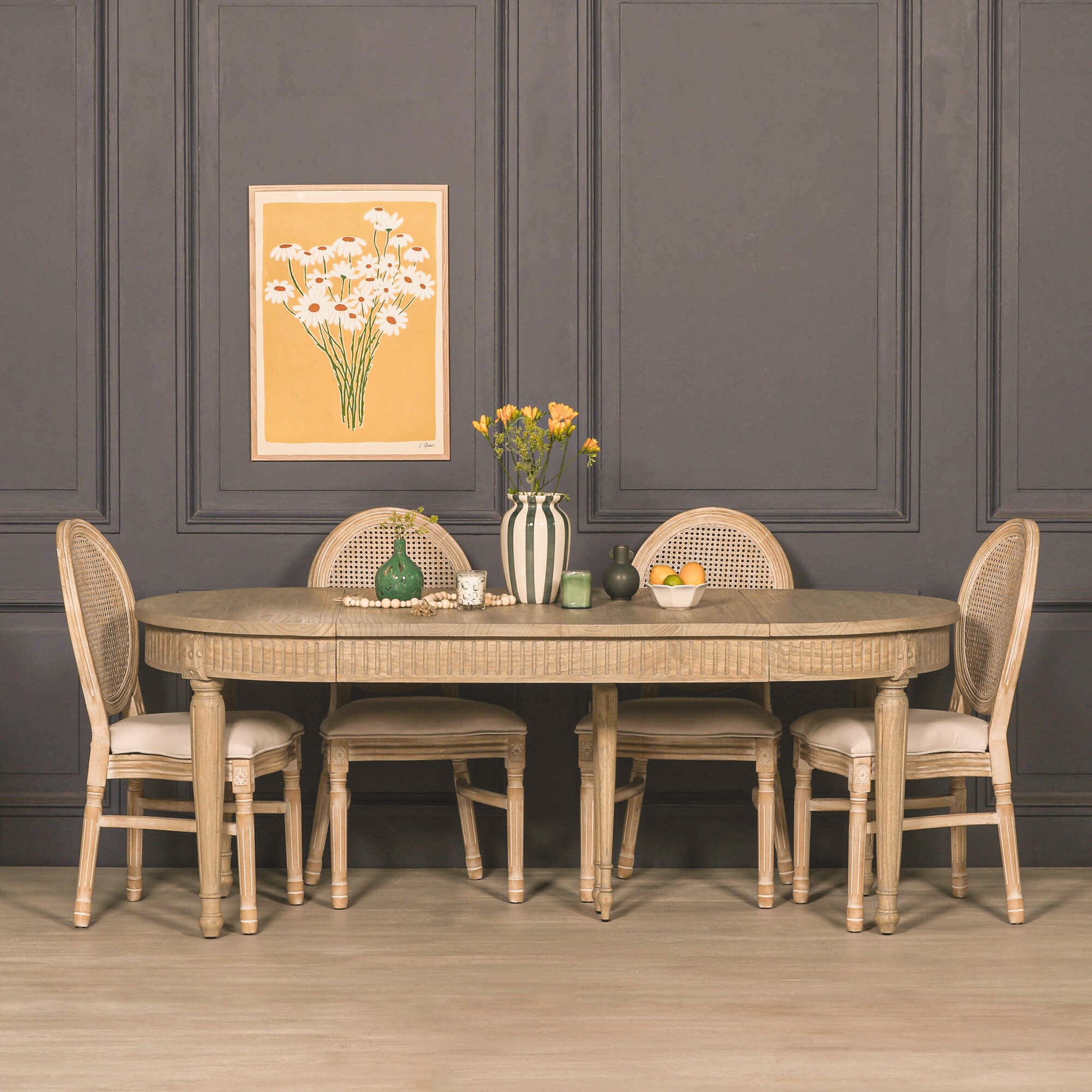 Camille White Cedar Wood Extendable Dining Table in a rustic finish styled with four upholstered rattan dining chairs in an elegant dining room, showcasing the extendable oval tabletop, carved apron detailing and seating for 4 to 8 people.