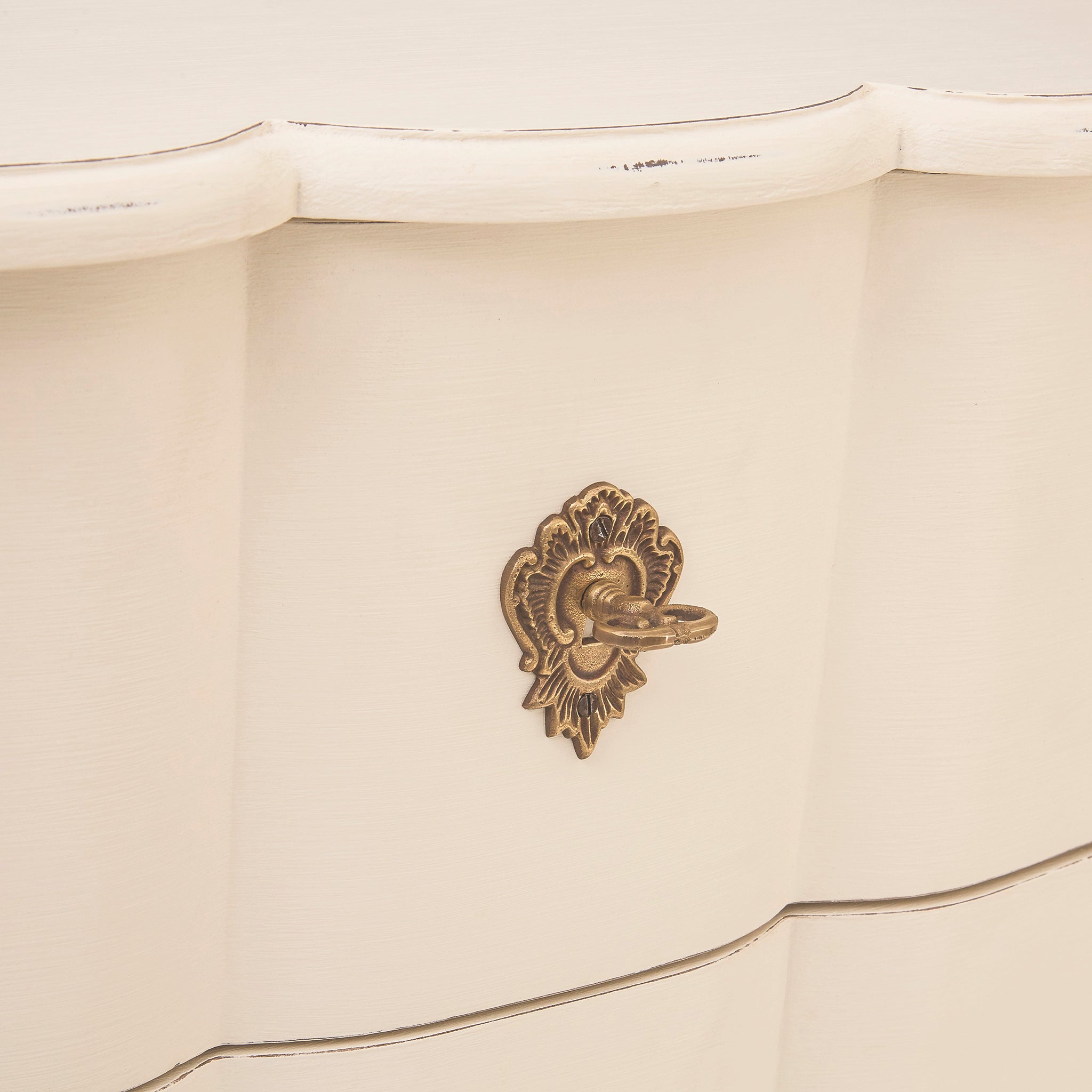 Close-up of an ornate antique brass drawer handle on the Camille white five drawer chest, highlighting the decorative metalwork, shaped drawer front and softly distressed painted finish.