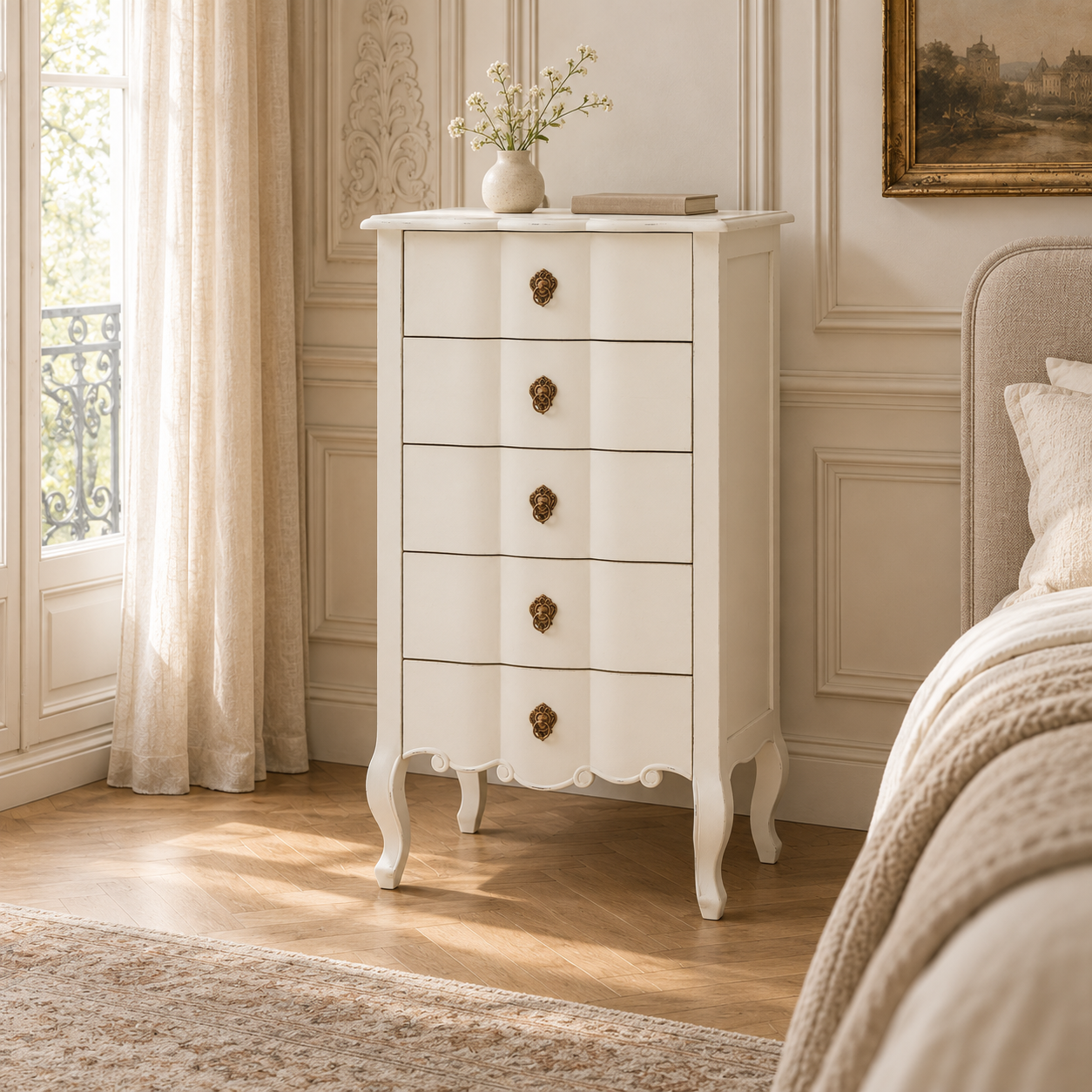 Camille white five-drawer chest with antique gold pulls in a sunlit bedroom beside a cream upholstered bed.