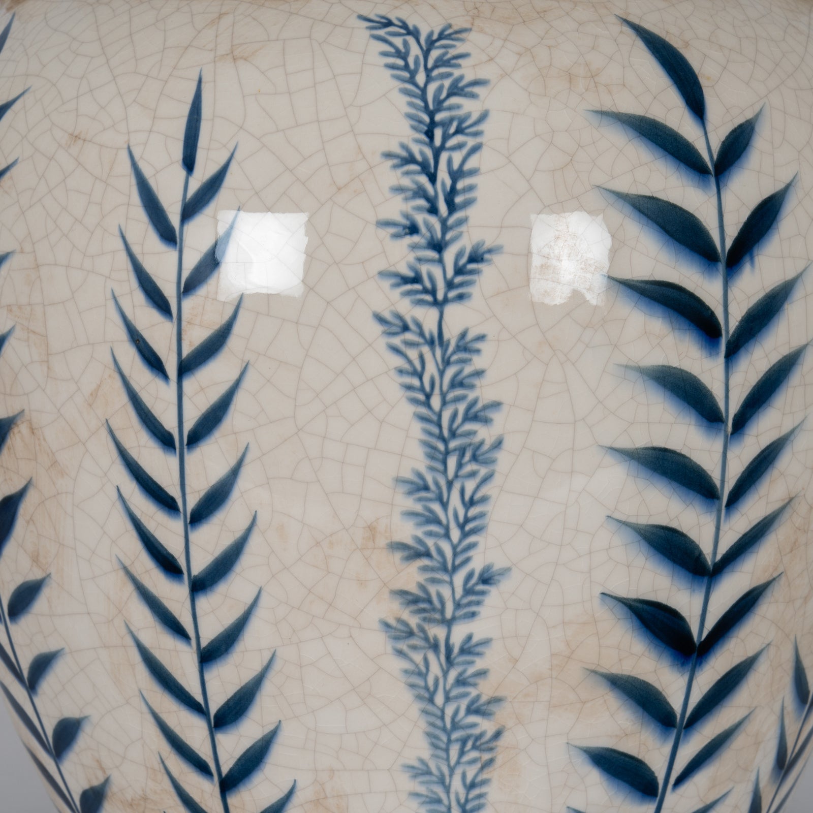 Close-up of Capucine ceramic vase showing blue botanical motifs and crackle glaze on a neutral background.