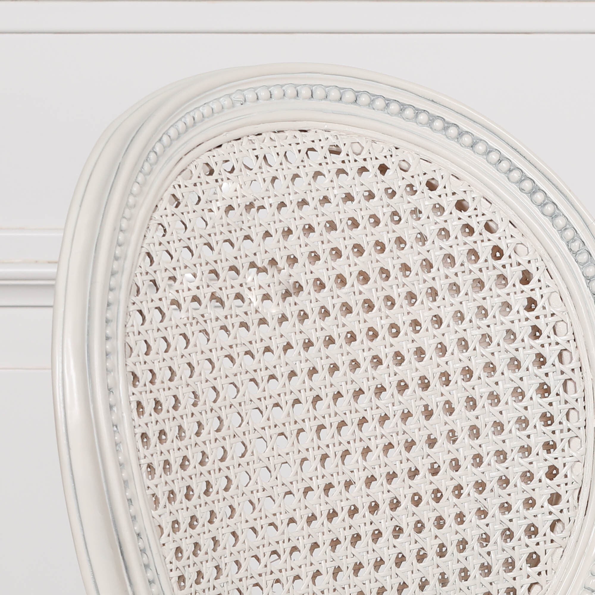 Extreme close-up of the Céleste French Chateau Rattan Dining Arm Chair highlighting the finely woven natural cane backrest, carved beaded oval frame and distressed off-white mahogany finish.
