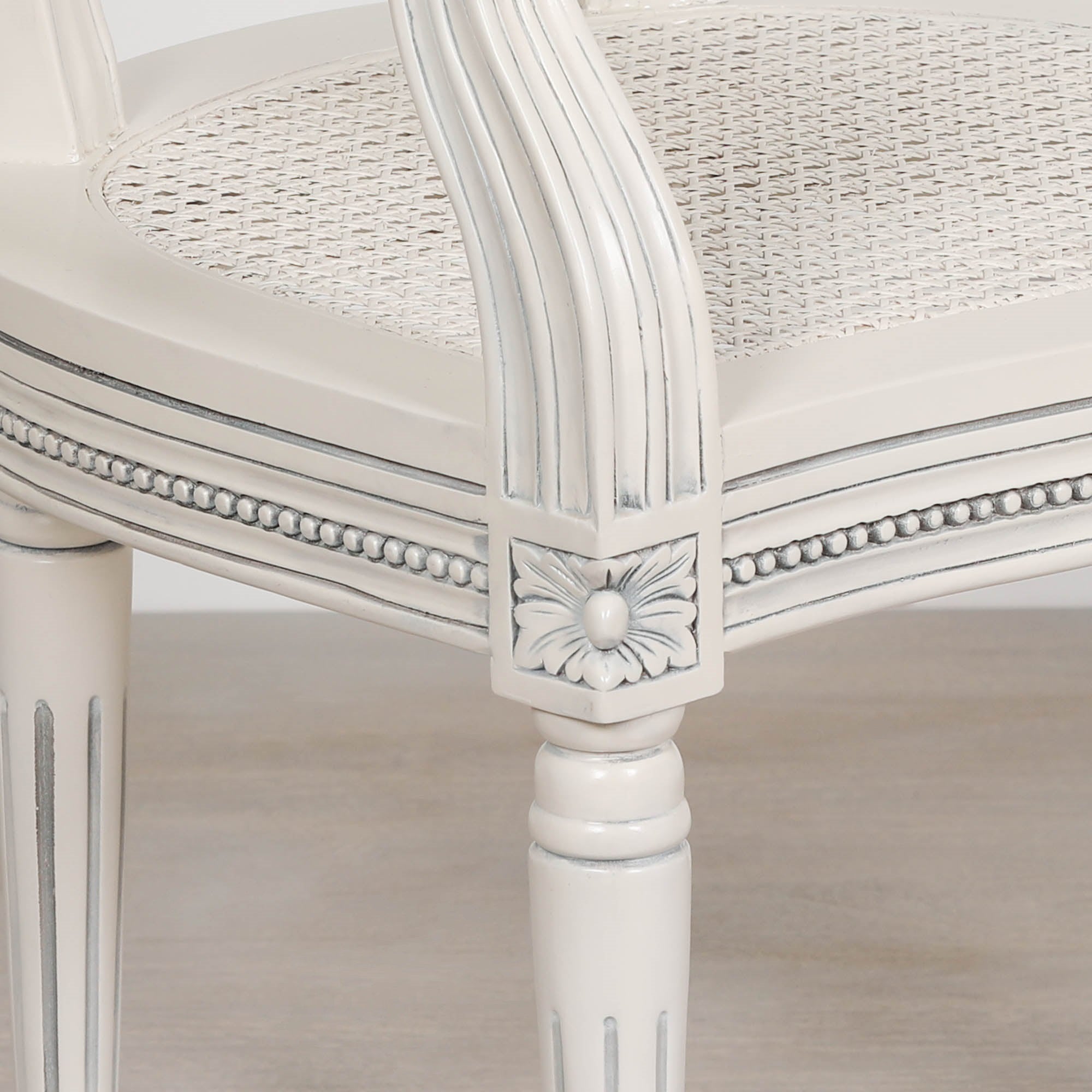 Detailed close-up of the Céleste French Chateau Rattan Dining Arm Chair showcasing the hand-carved floral corner detail, beaded trim, woven rattan seat and painted mahogany frame.