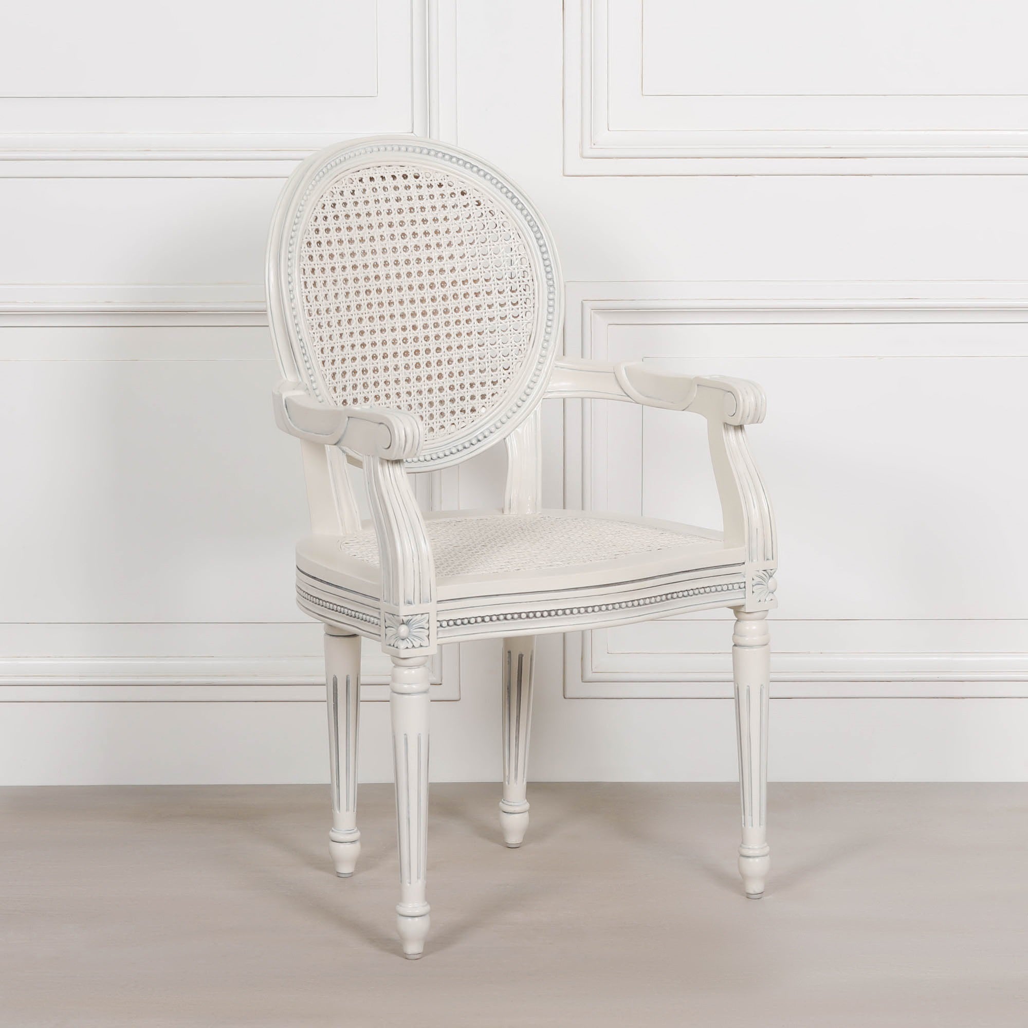 Three-quarter front view of the Céleste French Chateau Rattan Dining Arm Chair in Off-White Mahogany featuring carved scroll arms, woven cane back, natural rattan seat and timeless French country elegance.