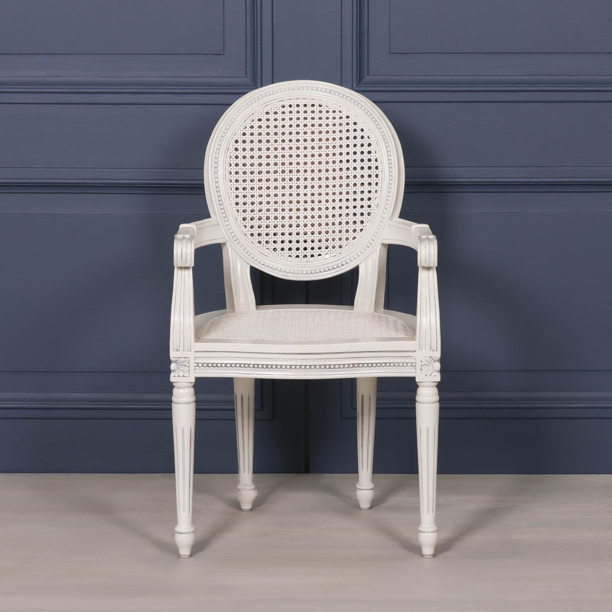 Front view of the Céleste French Chateau Rattan Dining Arm Chair in Off-White Mahogany showcasing its oval woven cane backrest, rattan seat, carved mahogany frame and elegant French Chateau design.