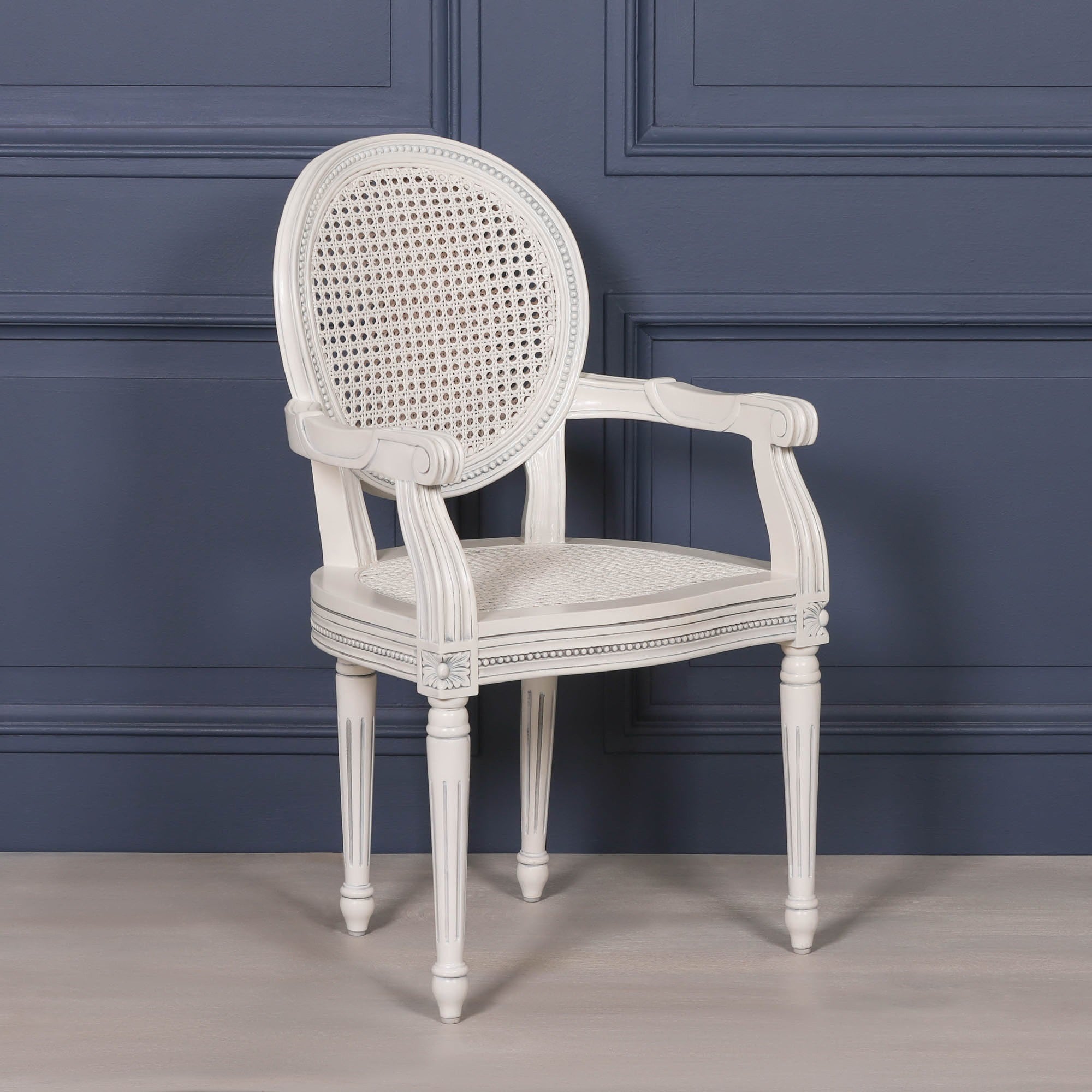 Angled front view of the Céleste French Chateau Rattan Dining Arm Chair in Off-White Mahogany featuring a hand-carved mahogany frame, woven natural rattan seat and backrest, elegant scroll arms and classic French country styling.