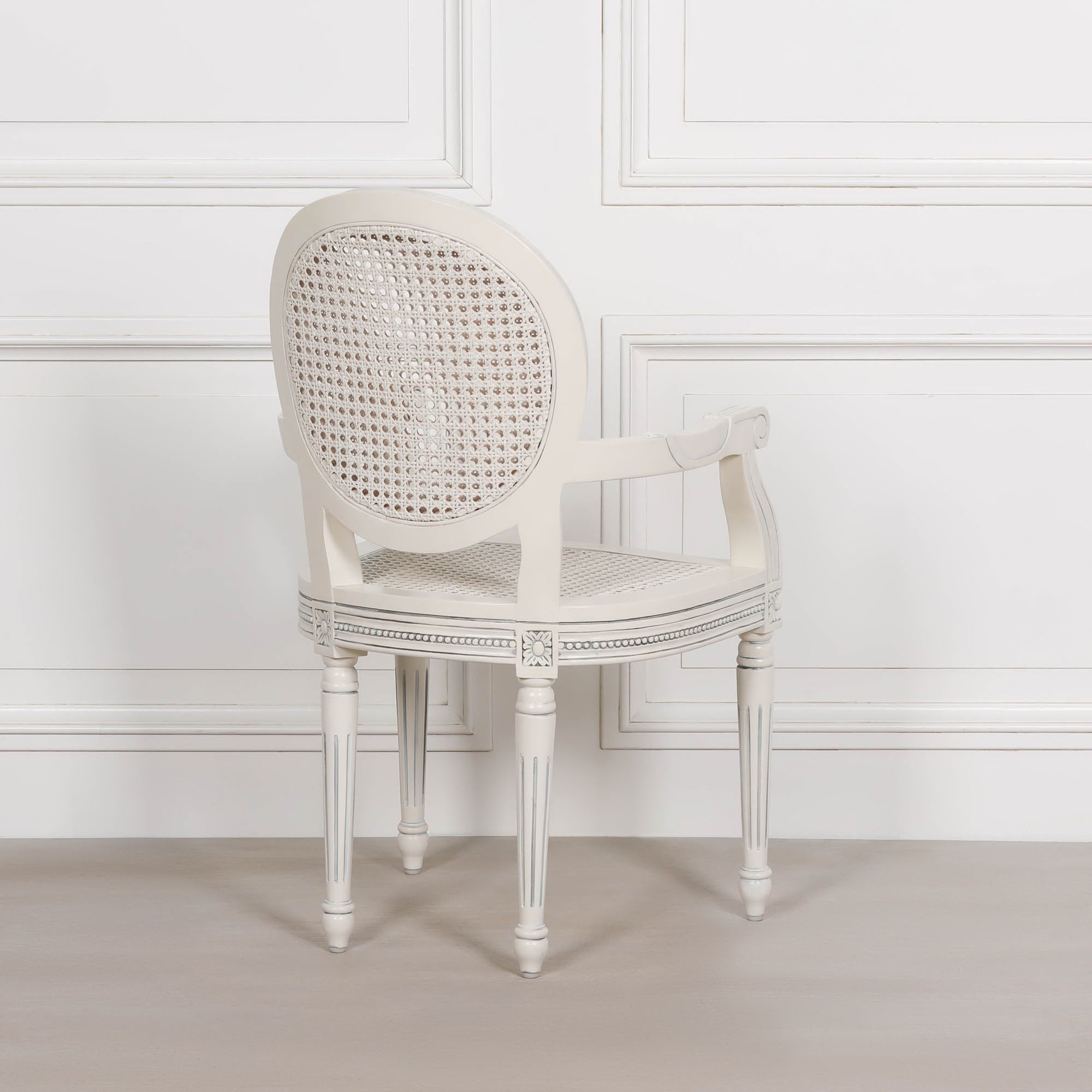 Rear angled view of the Céleste French Chateau Rattan Dining Arm Chair in Off-White Mahogany displaying its oval cane backrest, carved mahogany frame, woven rattan seat and elegant French Chateau silhouette.