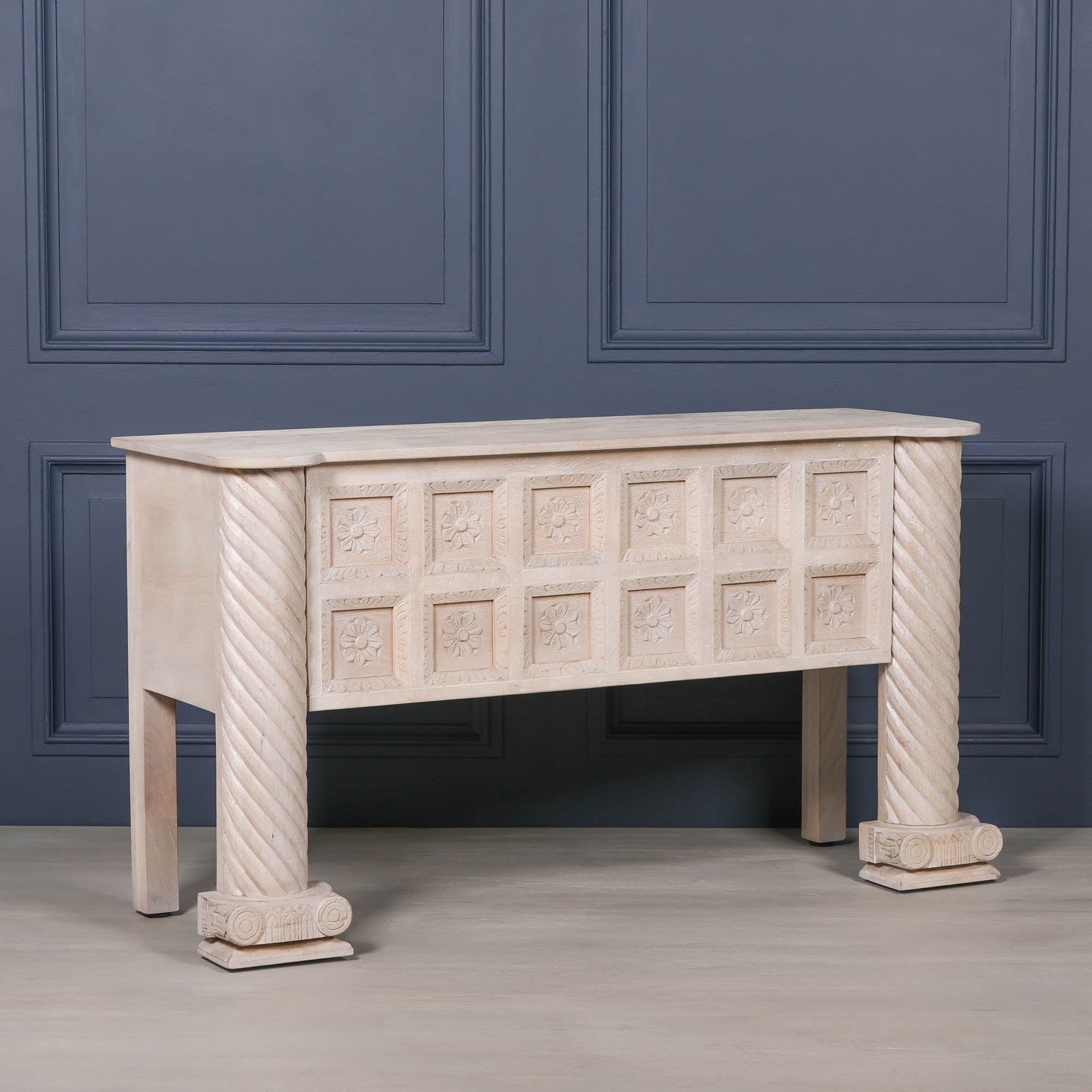 Angled view of Delphine carved mango wood reception desk with floral panels against a dark blue panelled wall