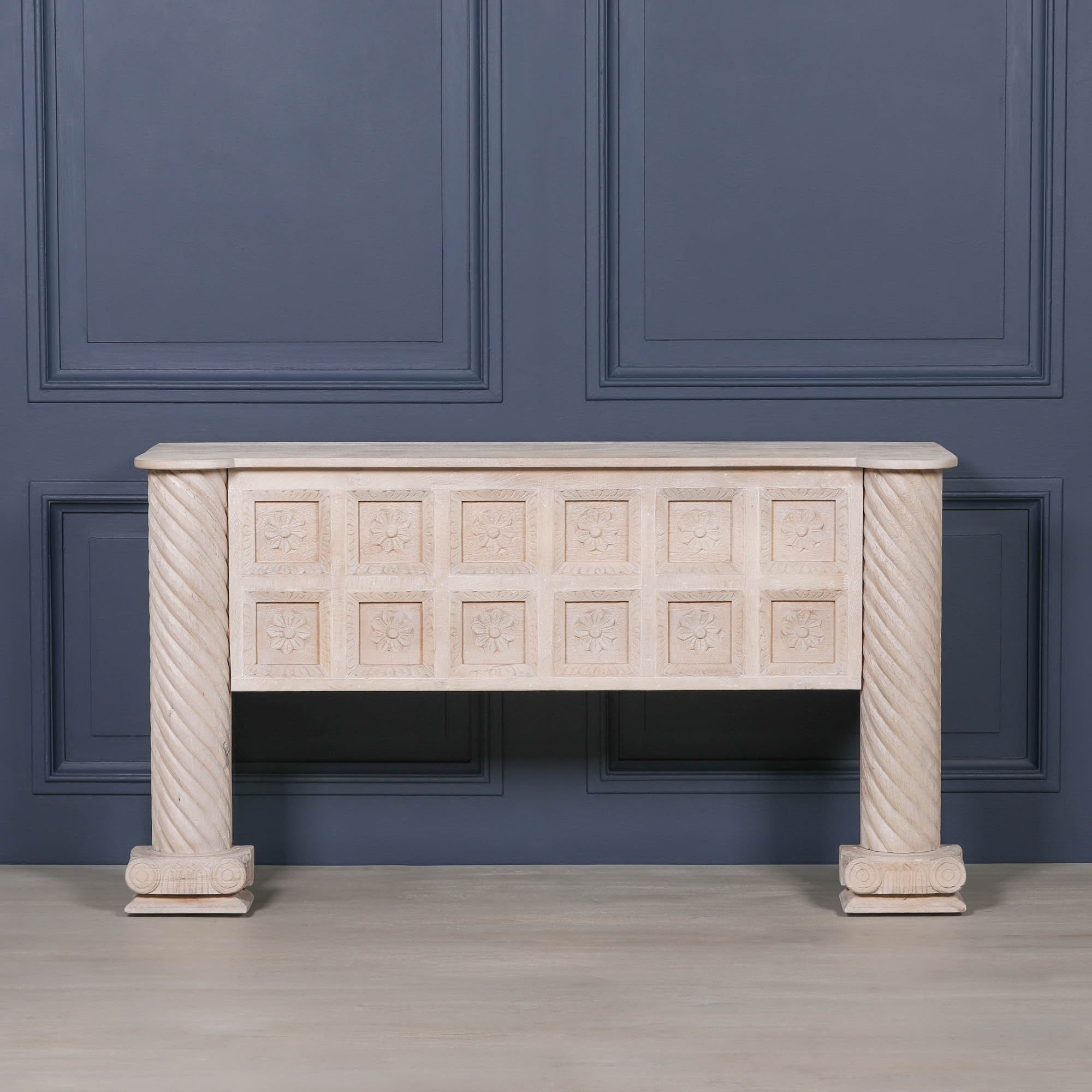 Front view of Delphine carved mango wood reception desk with twisted columns against a dark blue panelled wall
