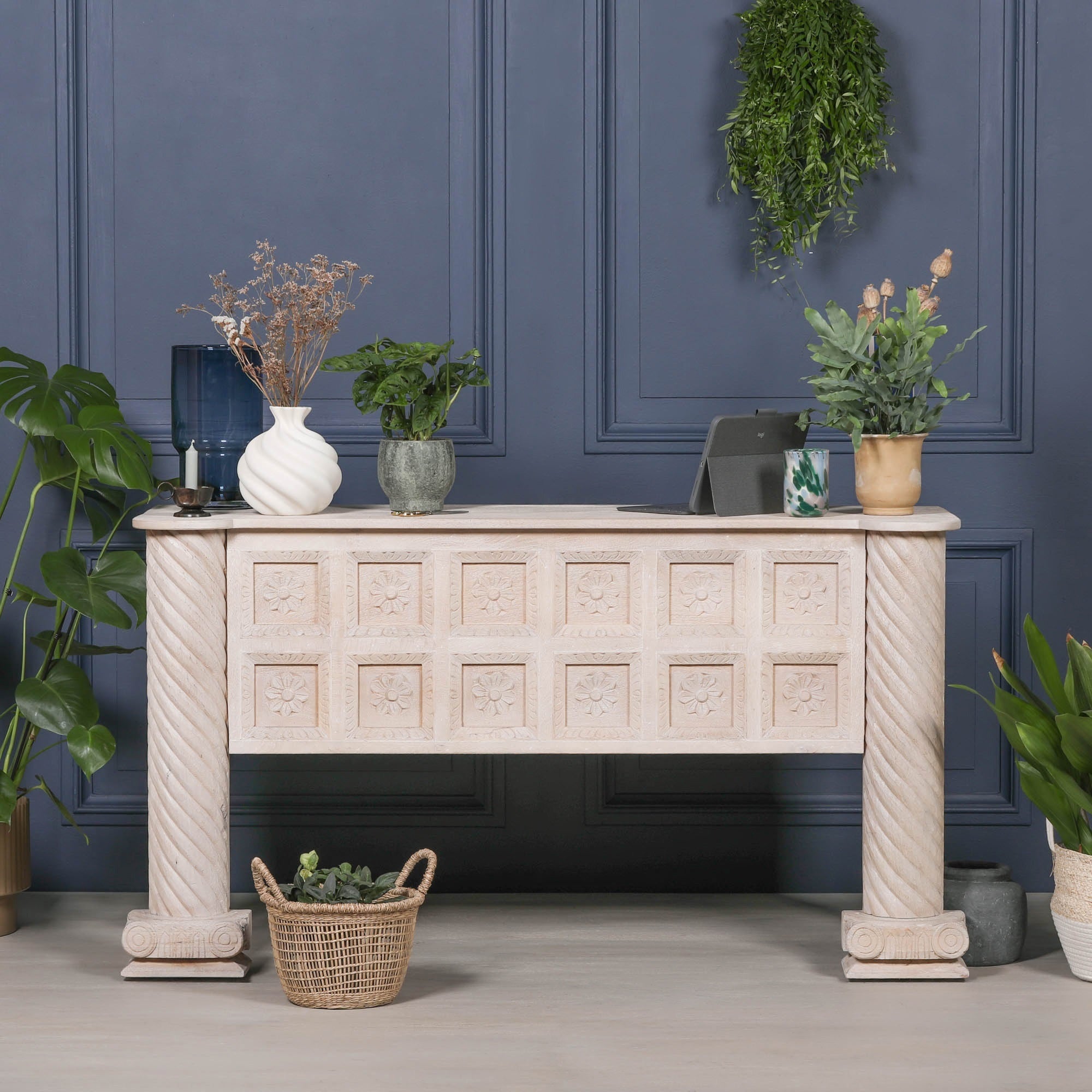 Delphine carved mango wood reception desk styled with plants against a dark blue panelled wall