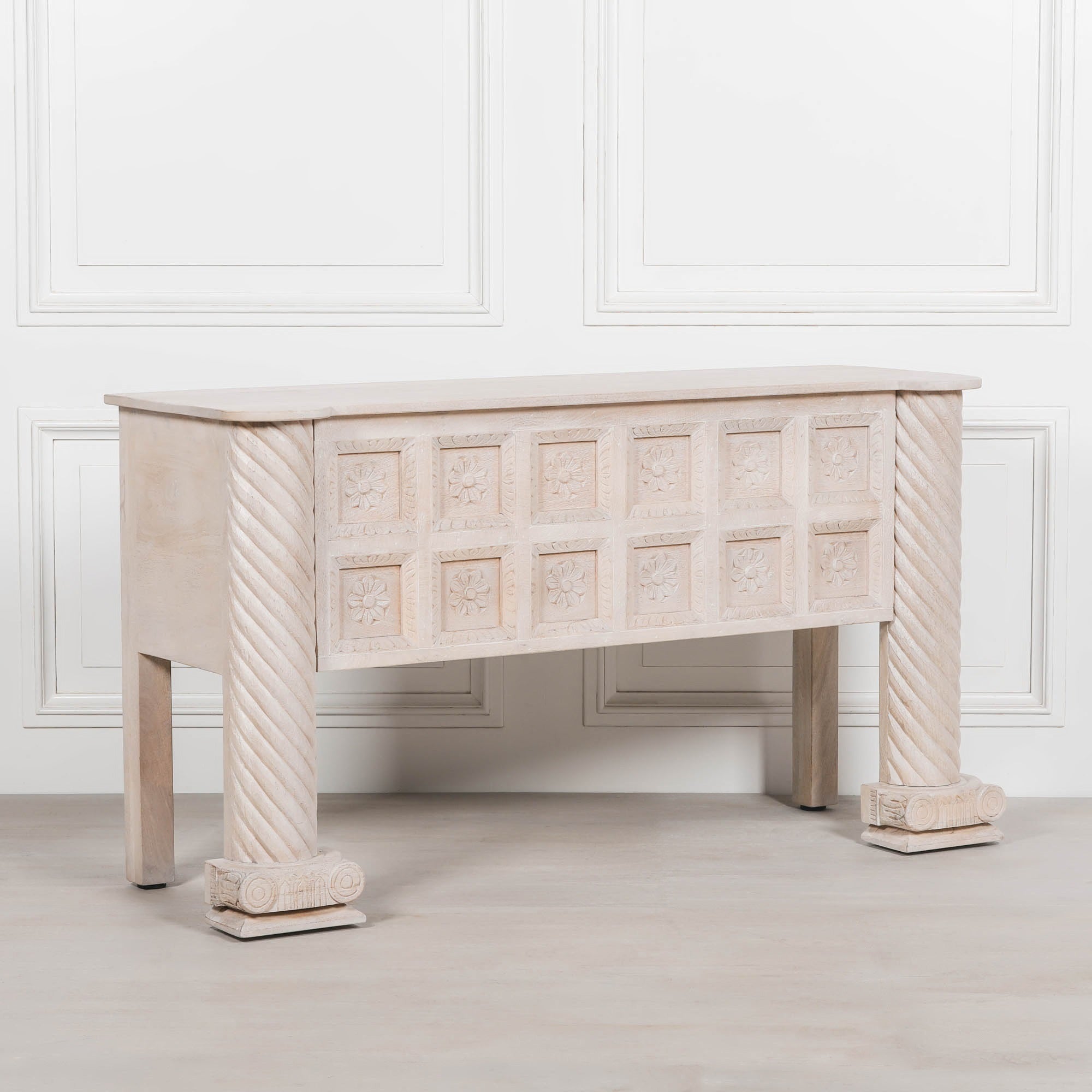 Angled view of Delphine carved mango wood reception desk with floral panels against a white panelled wall