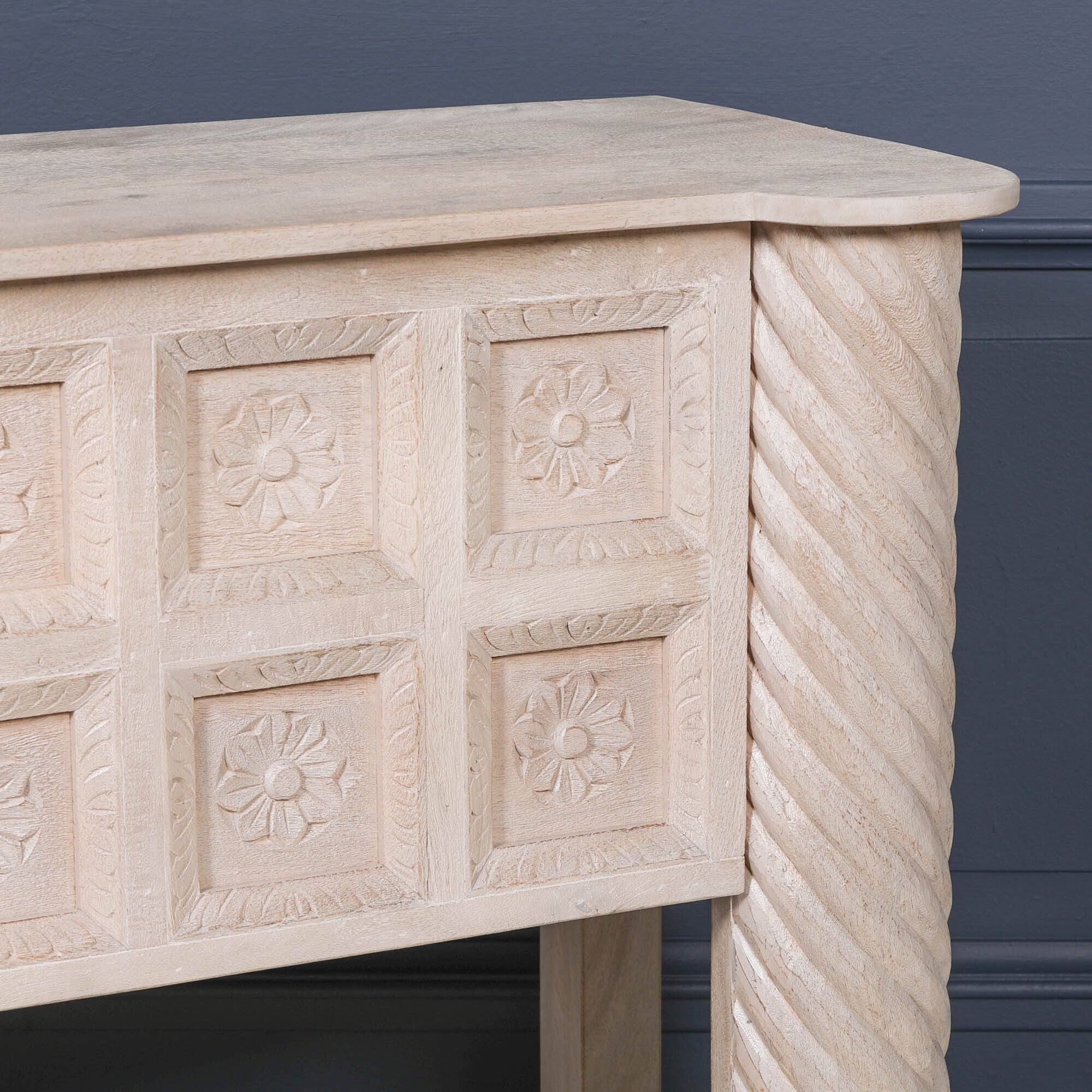 Close-up of Delphine mango wood reception desk with floral carving and twisted column against a dark blue wall