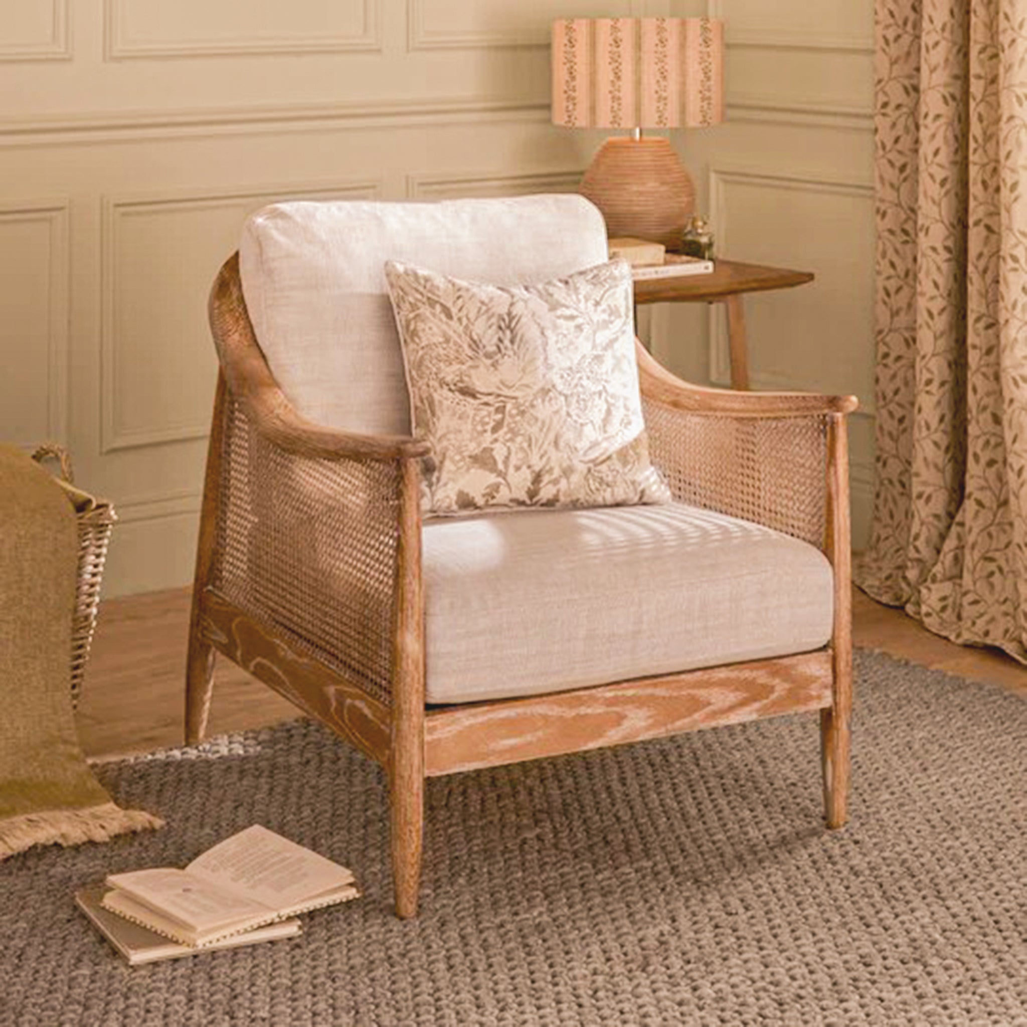 Elara French Style Rattan Accent Chair with Linen Seat styled in an elegant living room, featuring a natural oak frame, woven cane sides, soft linen upholstery and decorative cushion beside a side table and lamp.