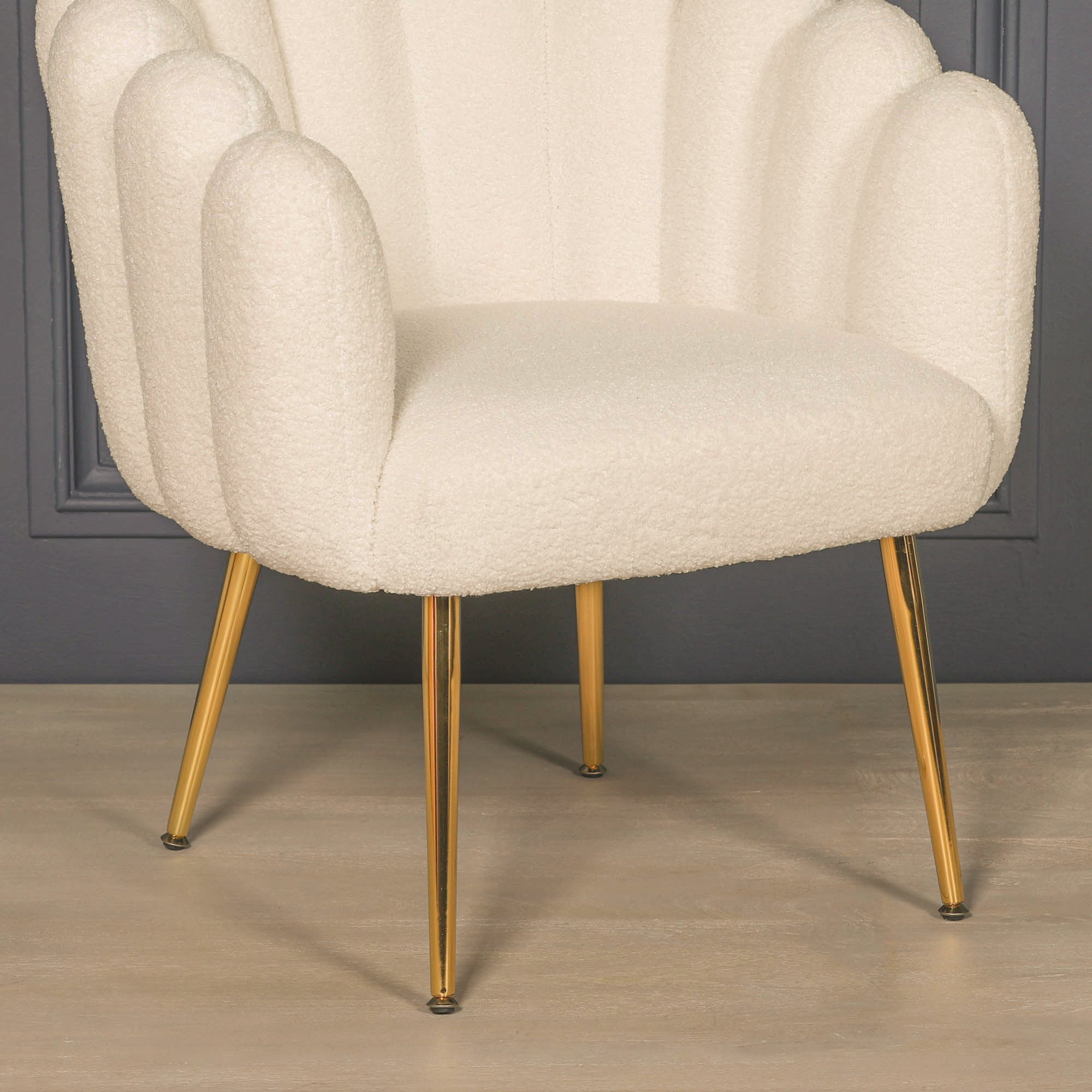 Close-up detail of the Elara Scalloped White Bouclé Dining Chair with Gold Metal Legs showcasing the plush upholstered seat, textured white bouclé fabric, sculptural scalloped backrest and polished tapered gold metal legs.