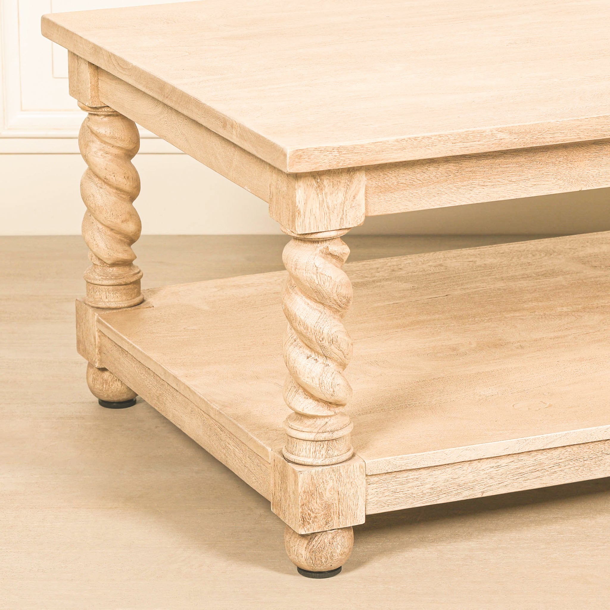 Detailed angled view of the Éloi acacia wood coffee table highlighting its thick rectangular tabletop, hand-carved spiral twirl legs, lower wooden shelf and distinctive sculptural construction.