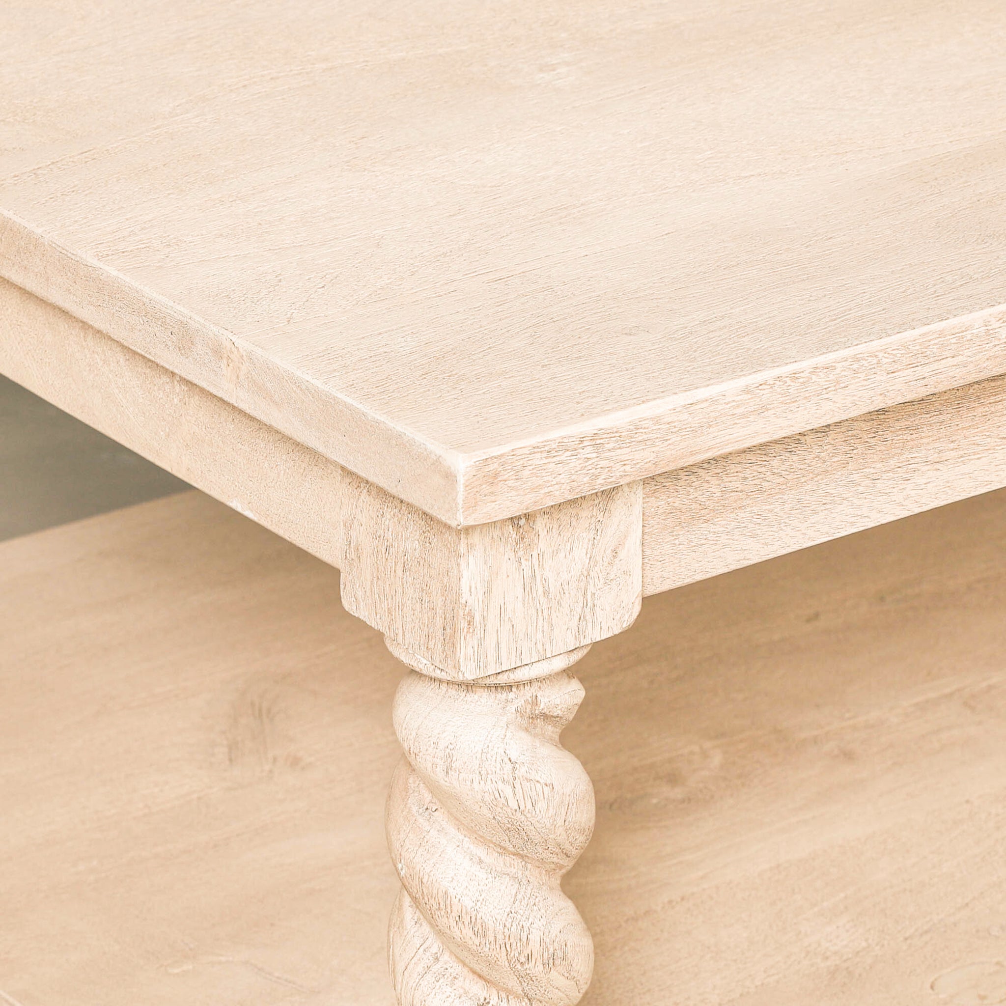Close-up of the Éloi acacia wood coffee table highlighting the natural wood grain and texture of the rectangular tabletop, substantial frame and distinctive hand-carved twisted twirl leg.