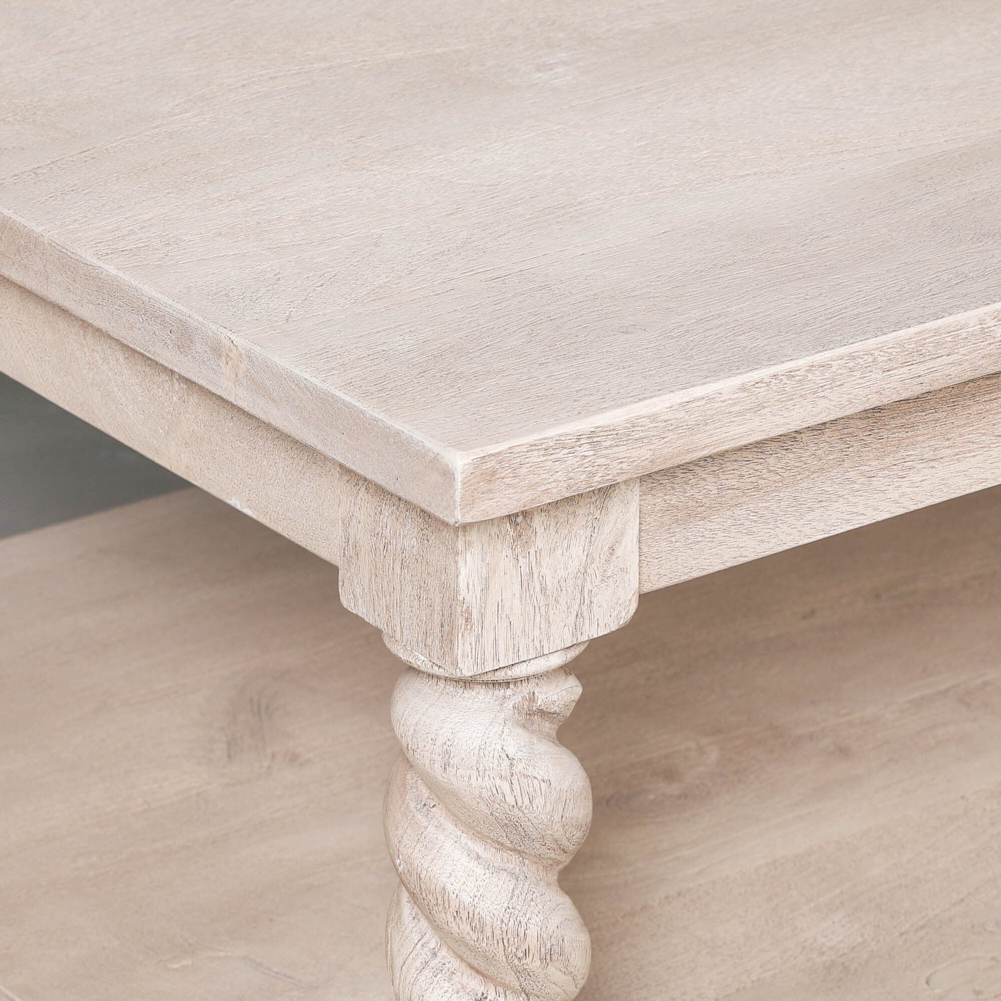 Close-up of Éloi acacia wood coffee table showing pale wood top and hand-carved twirl leg on a white background.