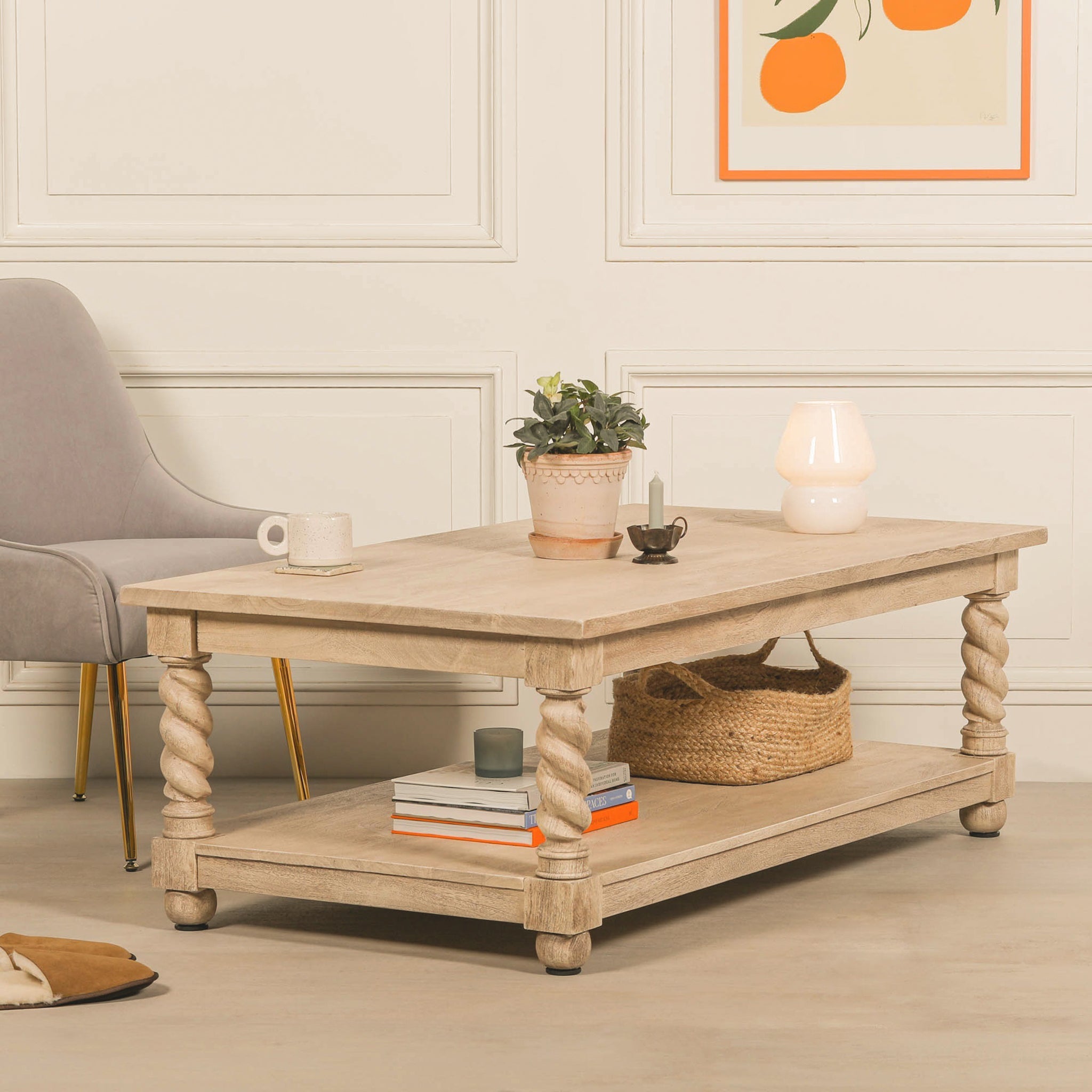 Éloi rectangular acacia wood coffee table styled with a lamp, plant and accessories, showcasing its natural light wood finish, sculptural hand-carved twirl legs and practical lower shelf.